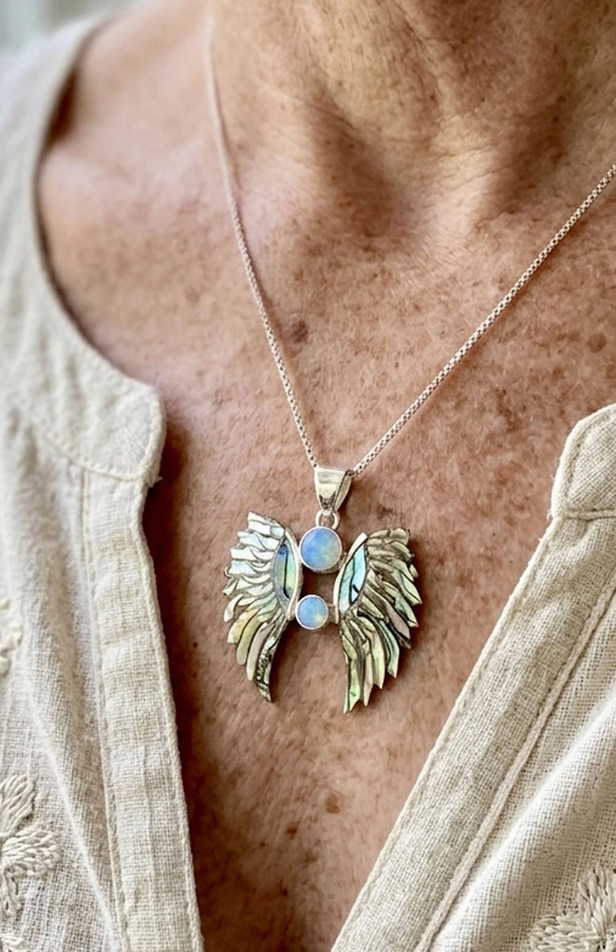 Sterling silver angel wings pendant featuring genuine opal gemstones and iridescent abalone shell, artisan handcrafted spiritual jewelry by Chantek Designs.