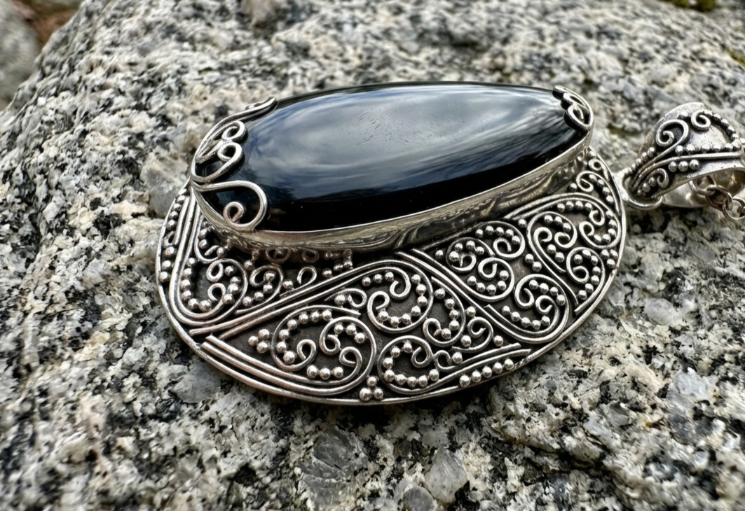 Handcrafted sterling silver pendant featuring a polished black onyx stone with ornate filigree sterling silver
