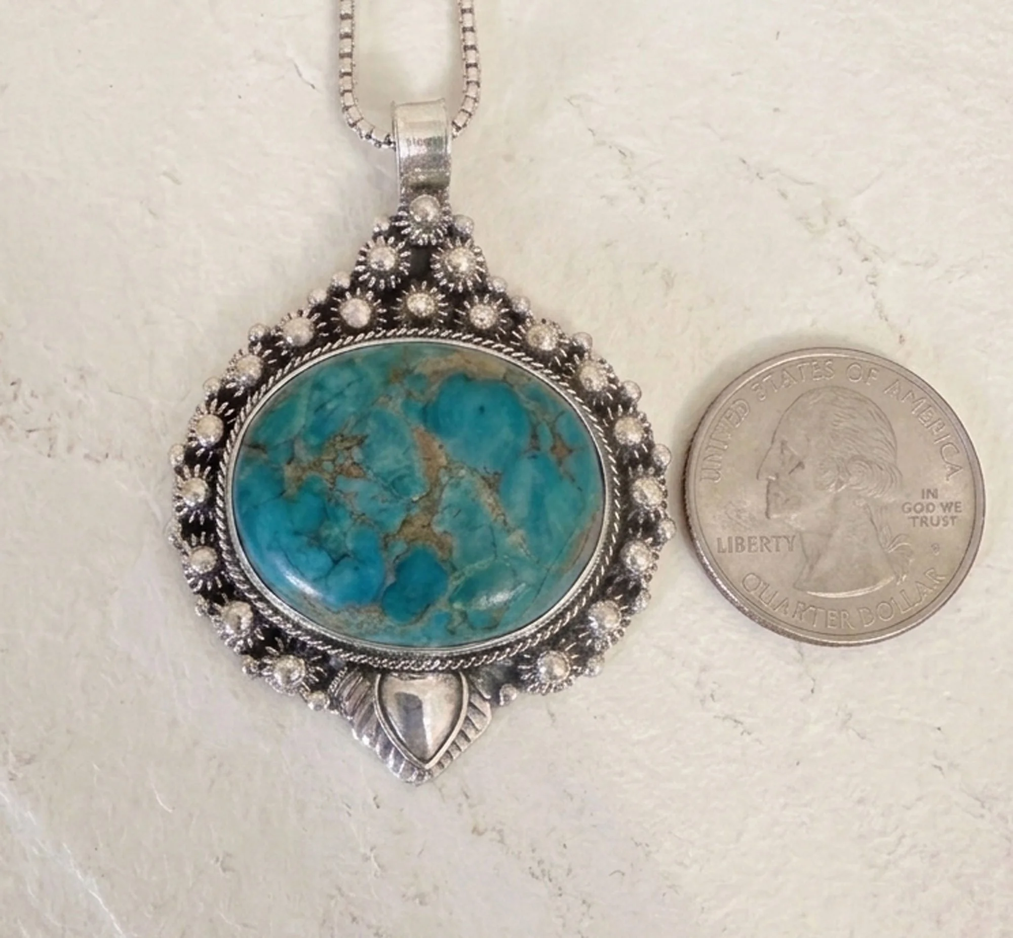 Natural turquoise pendant in sterling silver with Balinese detailing next to a quarter
