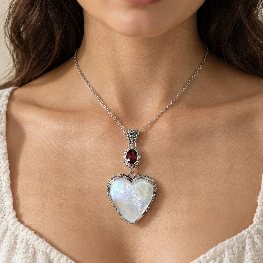 Mother of pearl heart pendant with red garnet and ornate sterling silver bail, shown on a necklace worn at the neckline