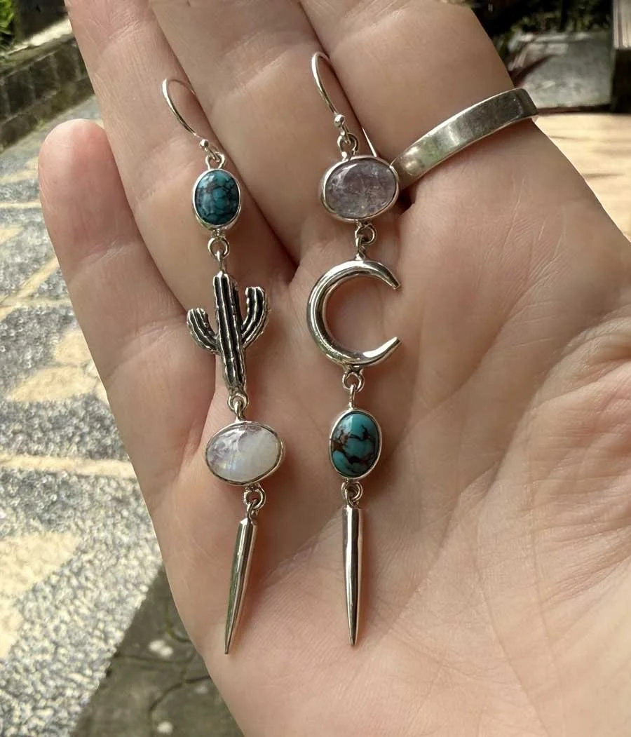 Handcrafted mismatched sterling silver earrings featuring turquoise, moonstone, with cactus and crescent moon designs. Unique boho artisan jewelry.