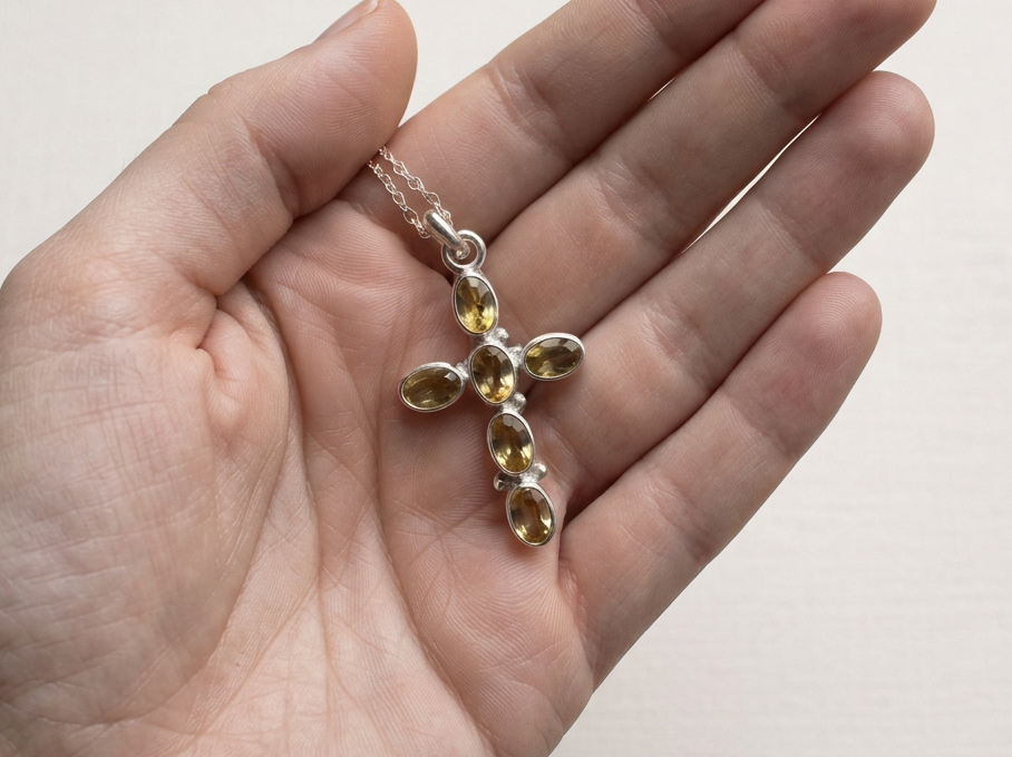 Citrine cross pendant with six oval golden gemstones set in sterling silver, shown in hand for scale