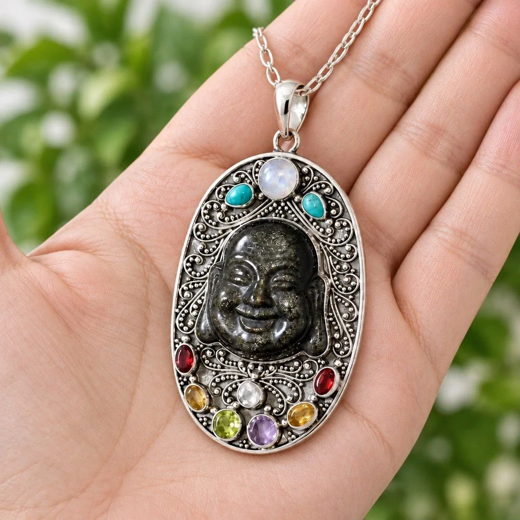 Hand holding an ornate obsidian Buddha pendant surrounded by colorful gemstones