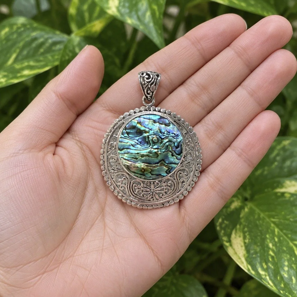 Double-sided abalone and Mother of Pearl sterling silver pendant handmade in Bali shown in hand for scale