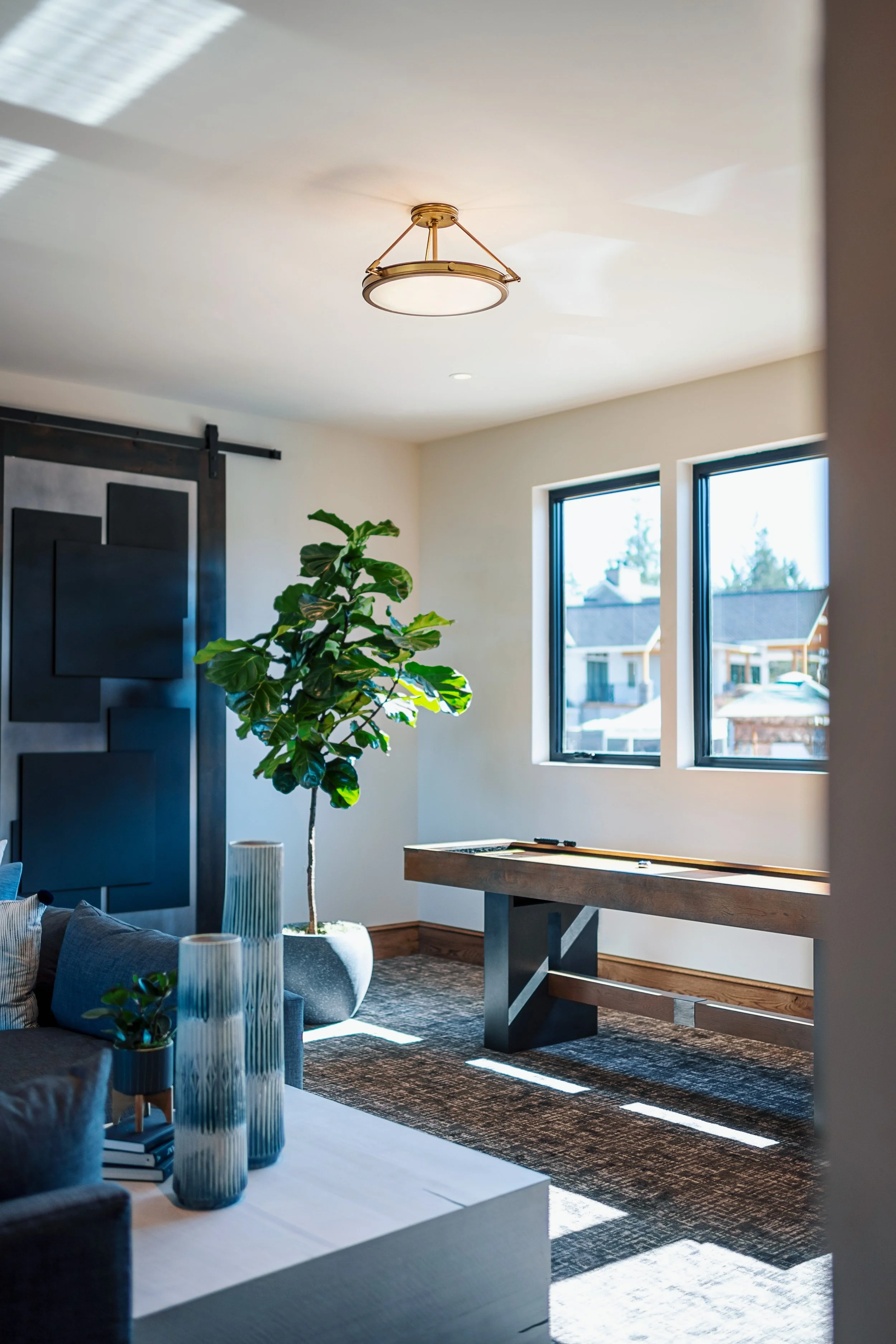 Modern living room with large window, green plant, wooden table, decorative vases, and sunlight casting shadows on the floor.