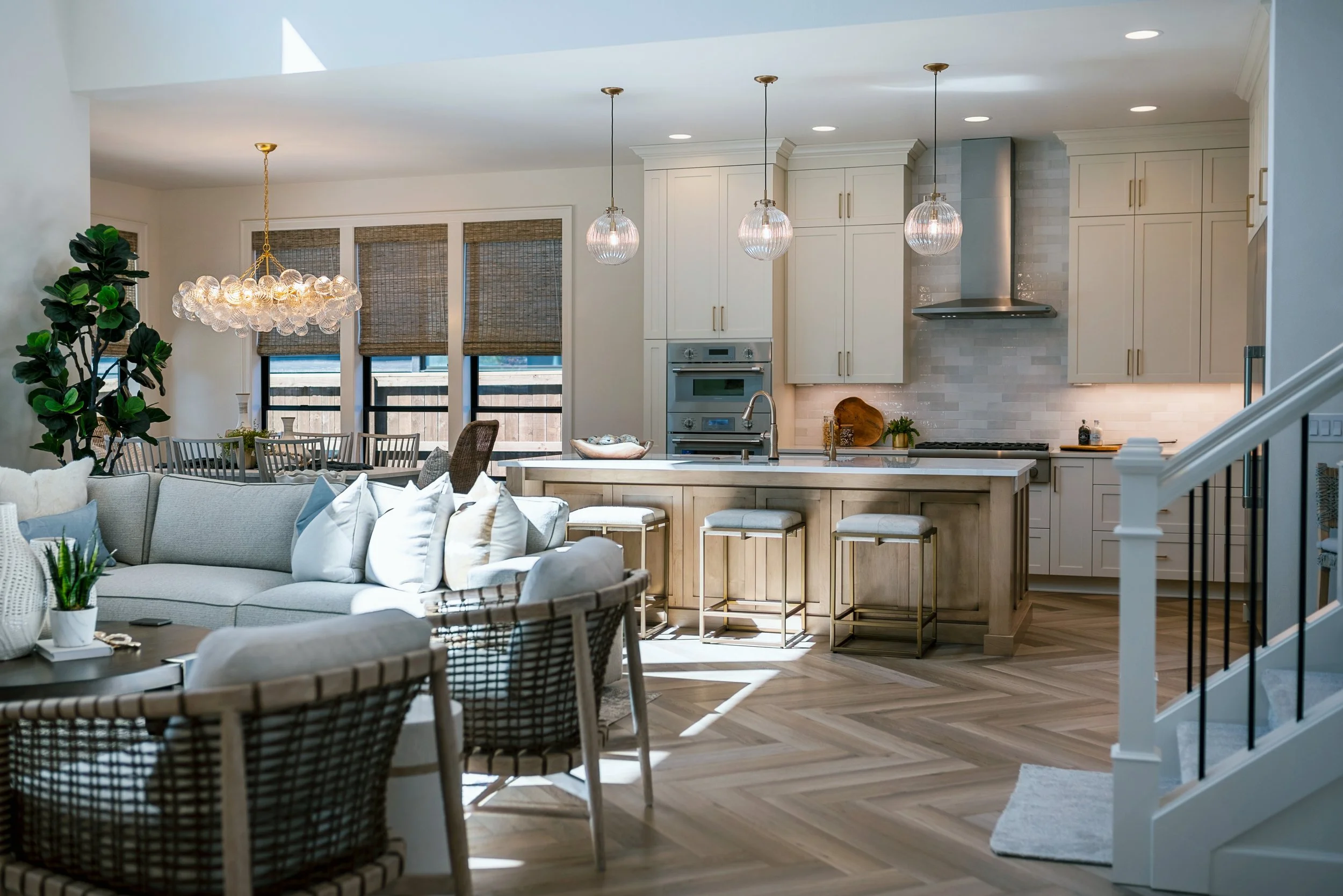 Open-concept living room and kitchen with white cabinetry, pendant lighting, and a large island with stools, natural light, and hardwood flooring.