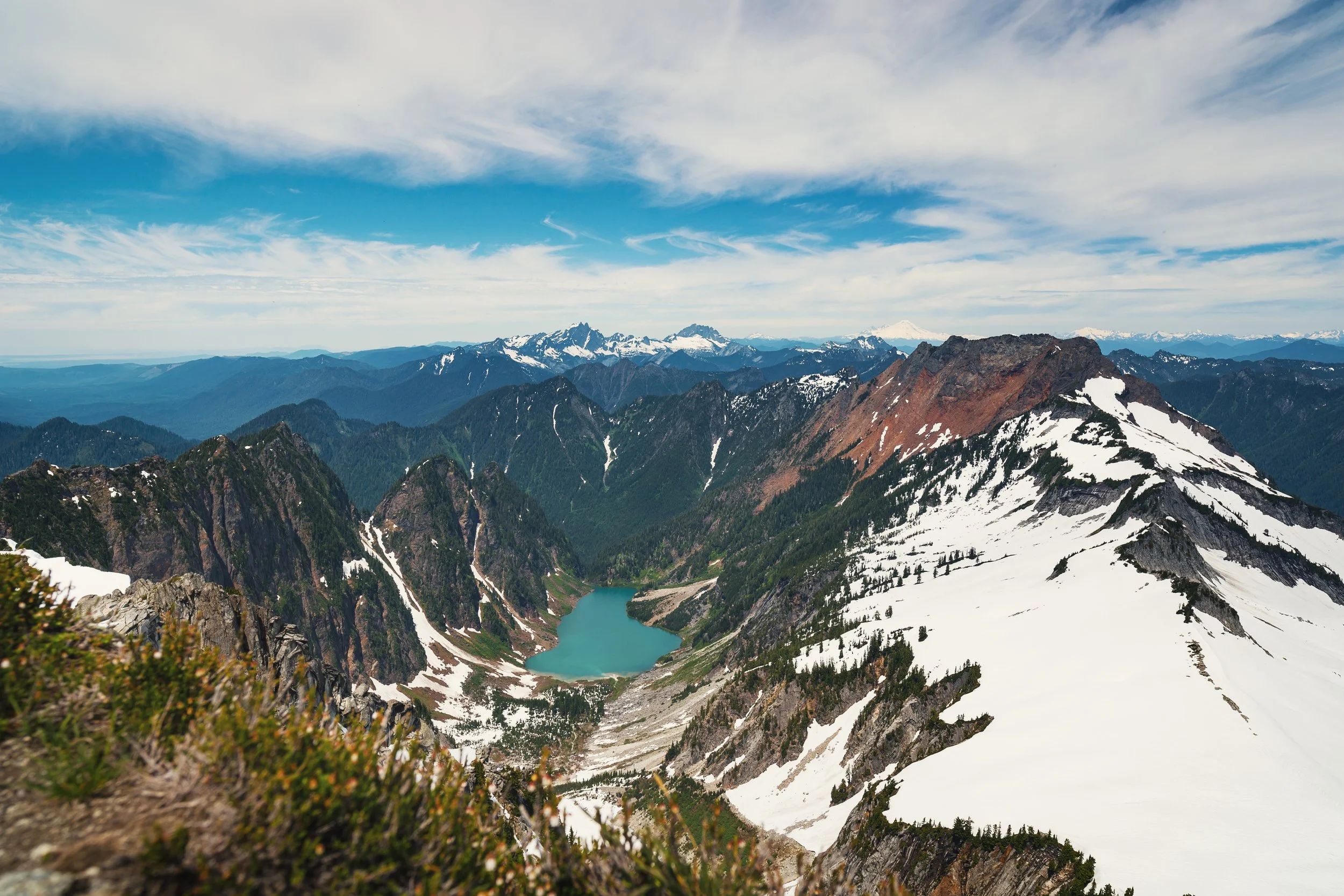 Snow-capped mountain peaks with a turquoise lake in the valley, partly cloudy blue sky.