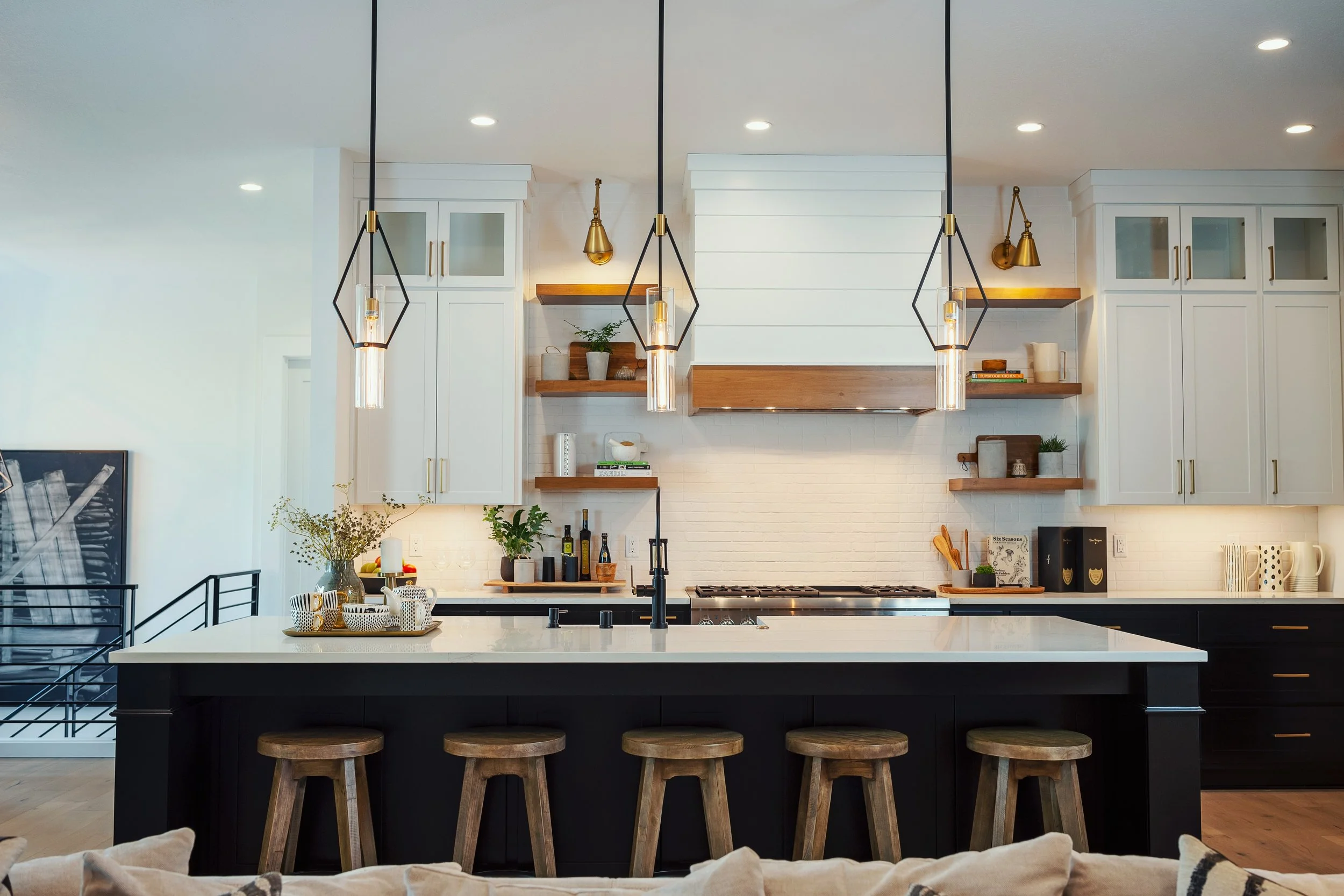 Modern kitchen with white cabinets, wooden open shelves, black island with bar stools, and pendant lights over the island.