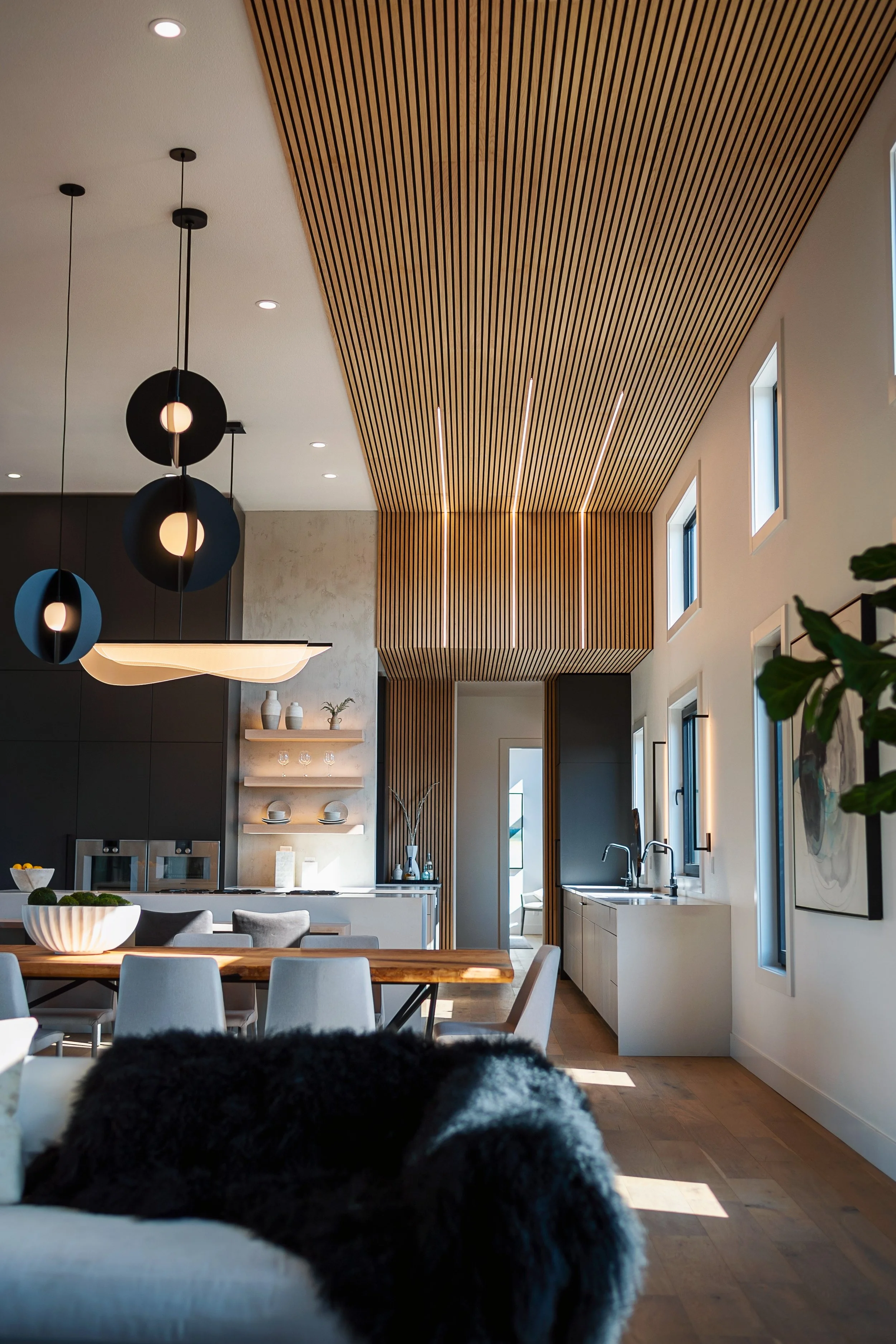 Modern kitchen with wood slat ceiling, pendant lights, white cabinetry, and windows.