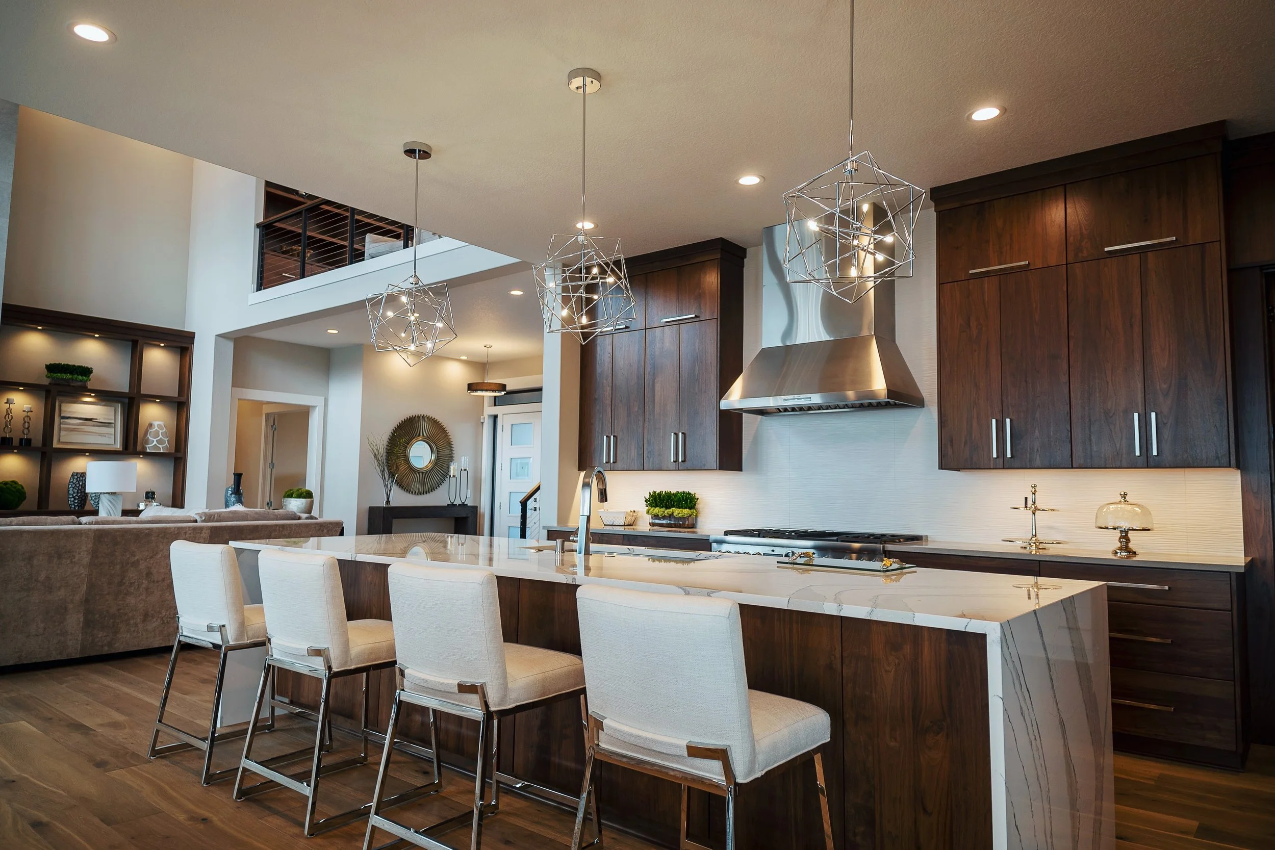 Modern open-concept kitchen with dark wood cabinets, a white marble island, pendant lights, and a dining area with white chairs.