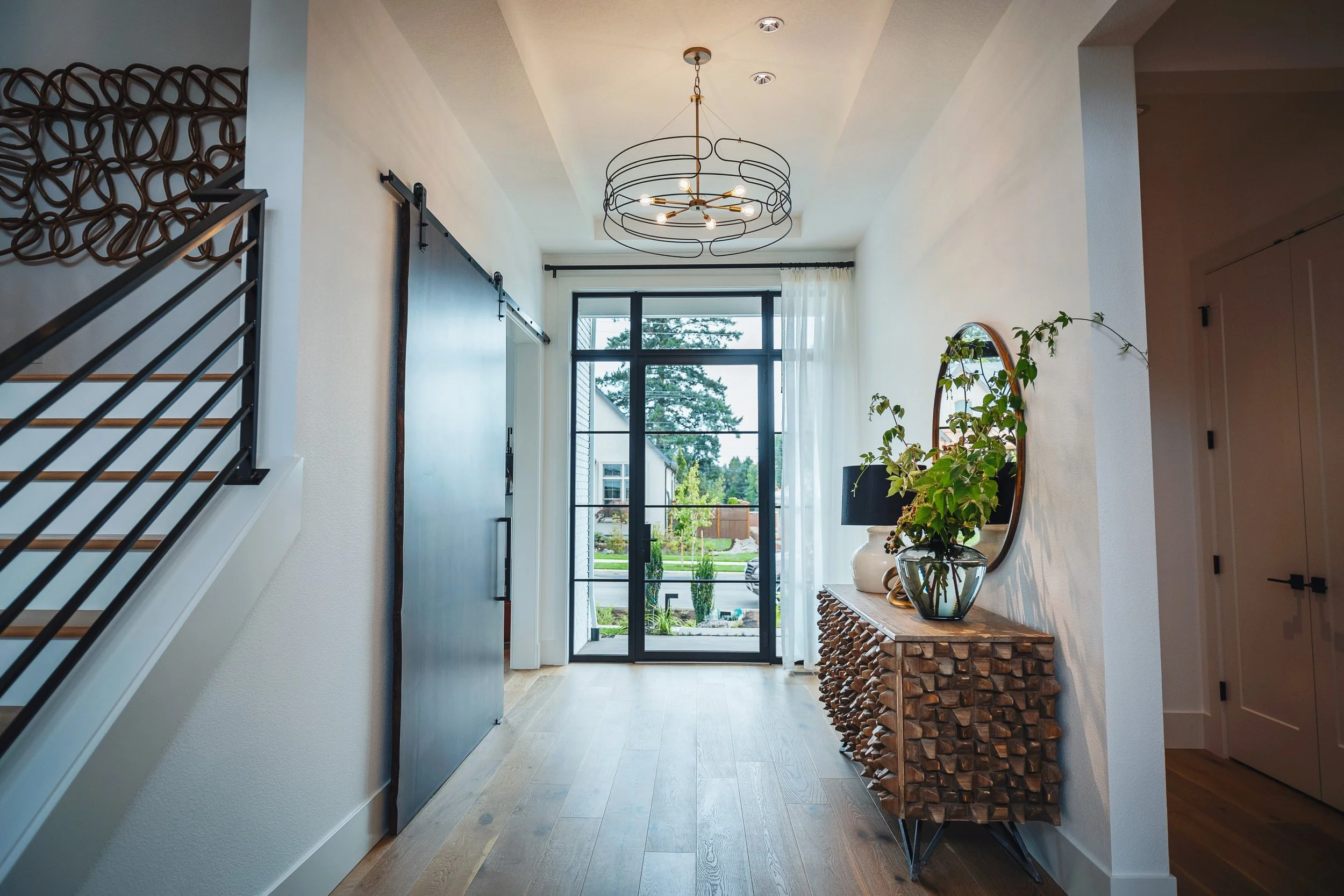 Hallway with large glass door and window, modern chandelier, plant on a wooden table, snow outside, minimalist decor.