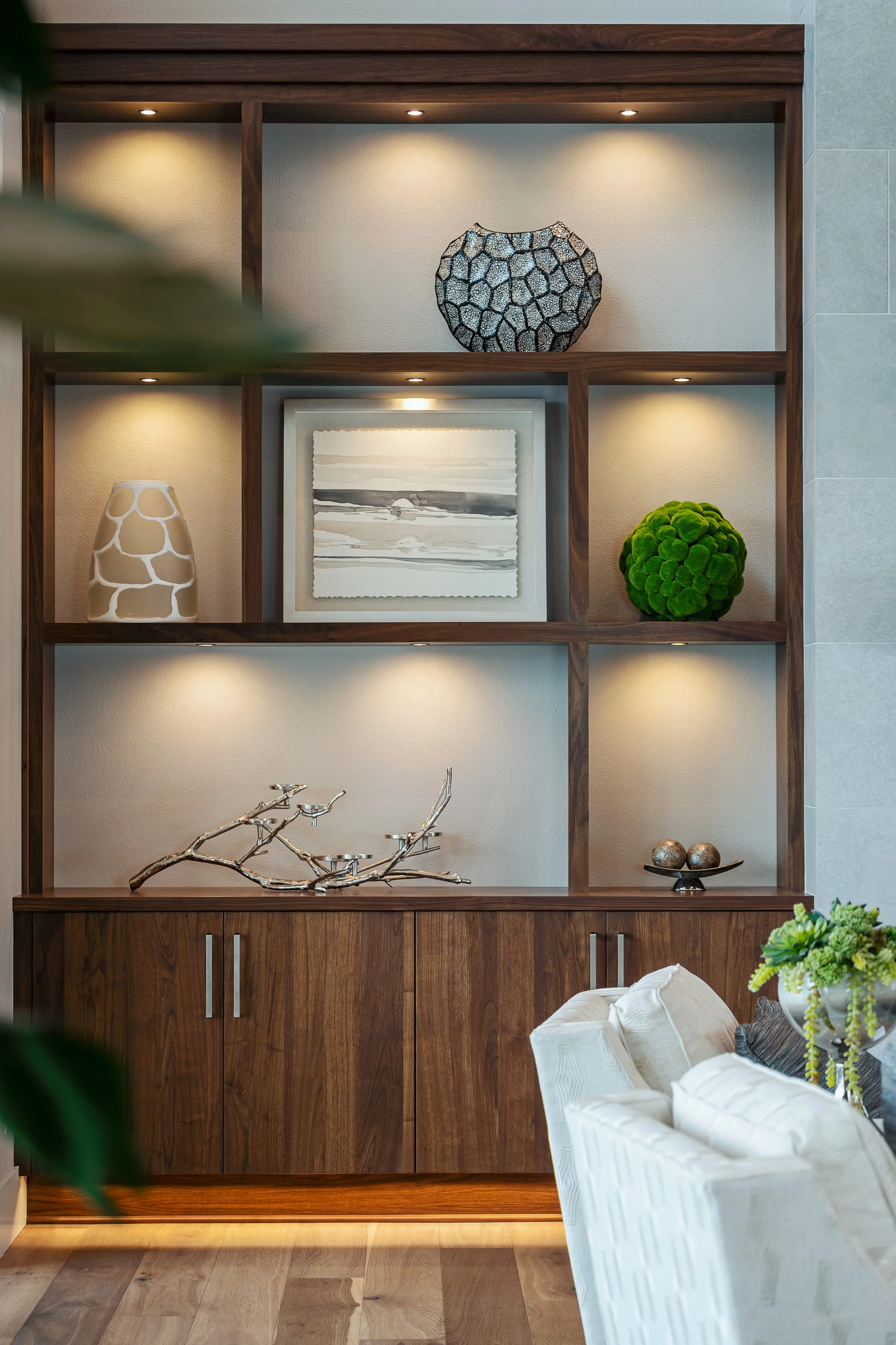 A wooden shelving unit with three decorative vases, a framed black and white landscape painting, and a green moss ball, with recessed lighting above.