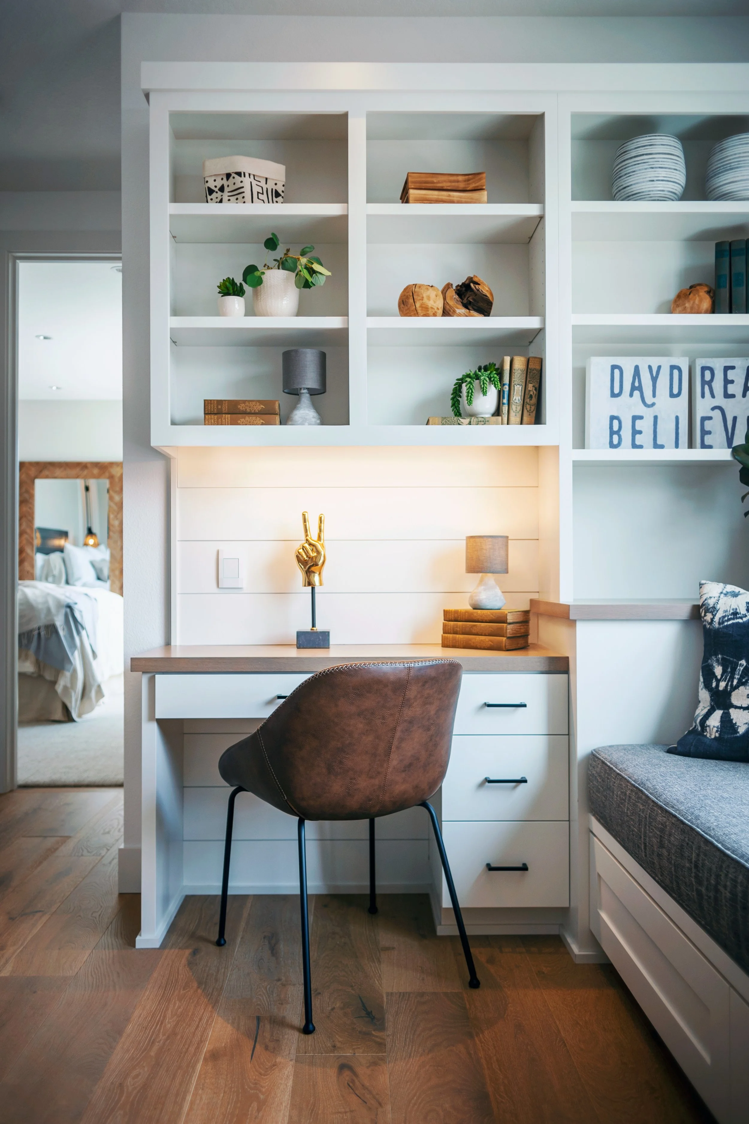 Home office nook with white desk and brown leather chair, decorative items, books, and a built-in bookshelf with vases, plants, and signs that say 'Daydream Believe.'