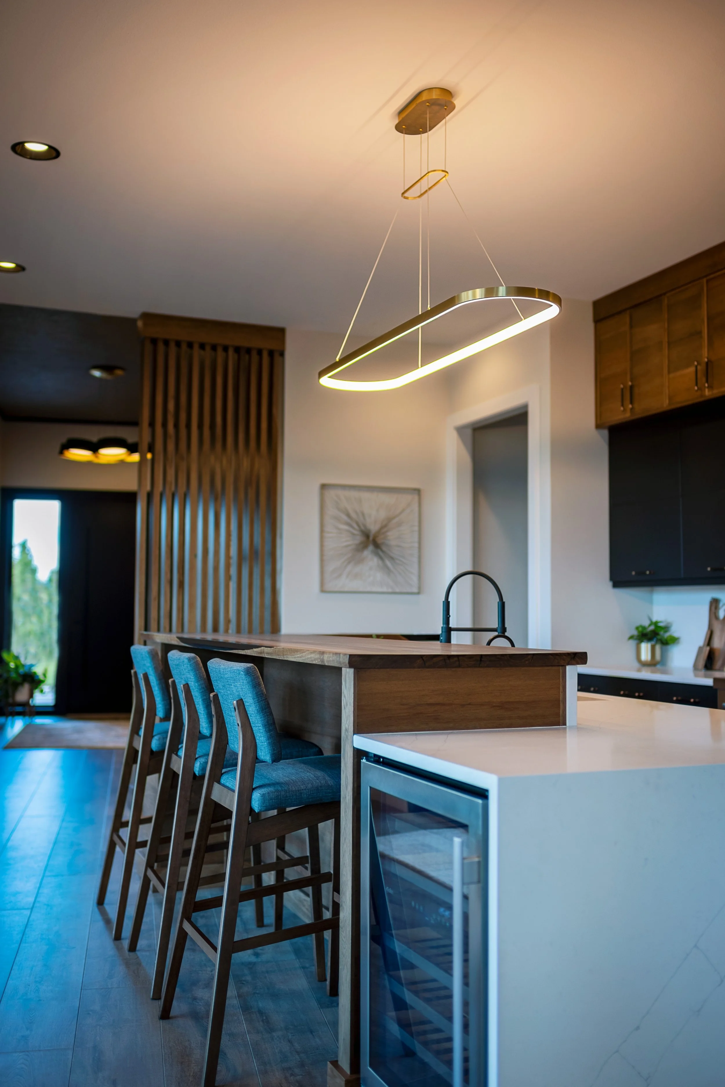 Modern kitchen with a white island, wooden barstools, wooden cabinets, and a unique oval-shaped pendant light hanging from the ceiling.