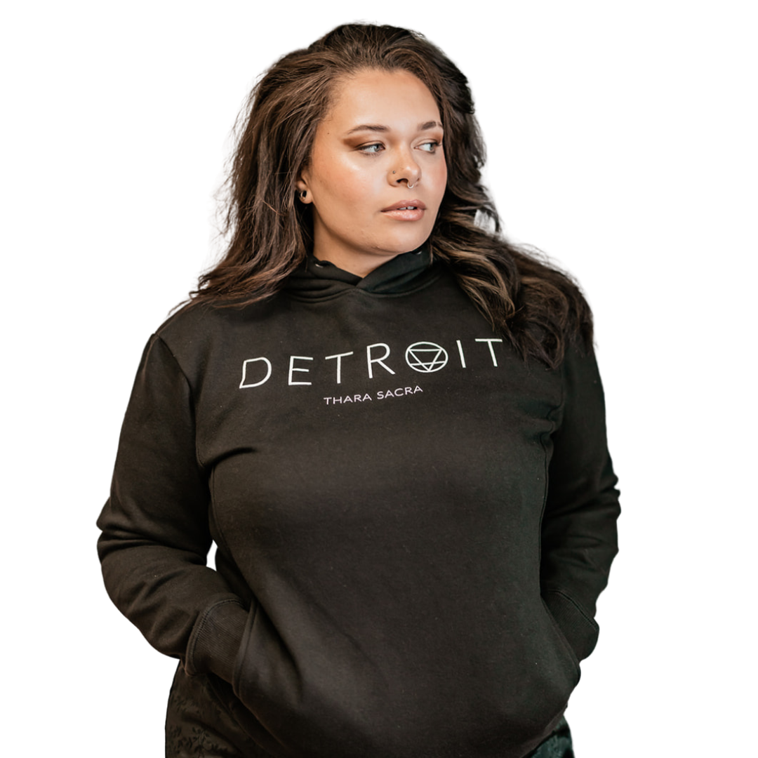 Woman wearing a black sweatshirt with the words Detroit and Thara Sacra on it in white