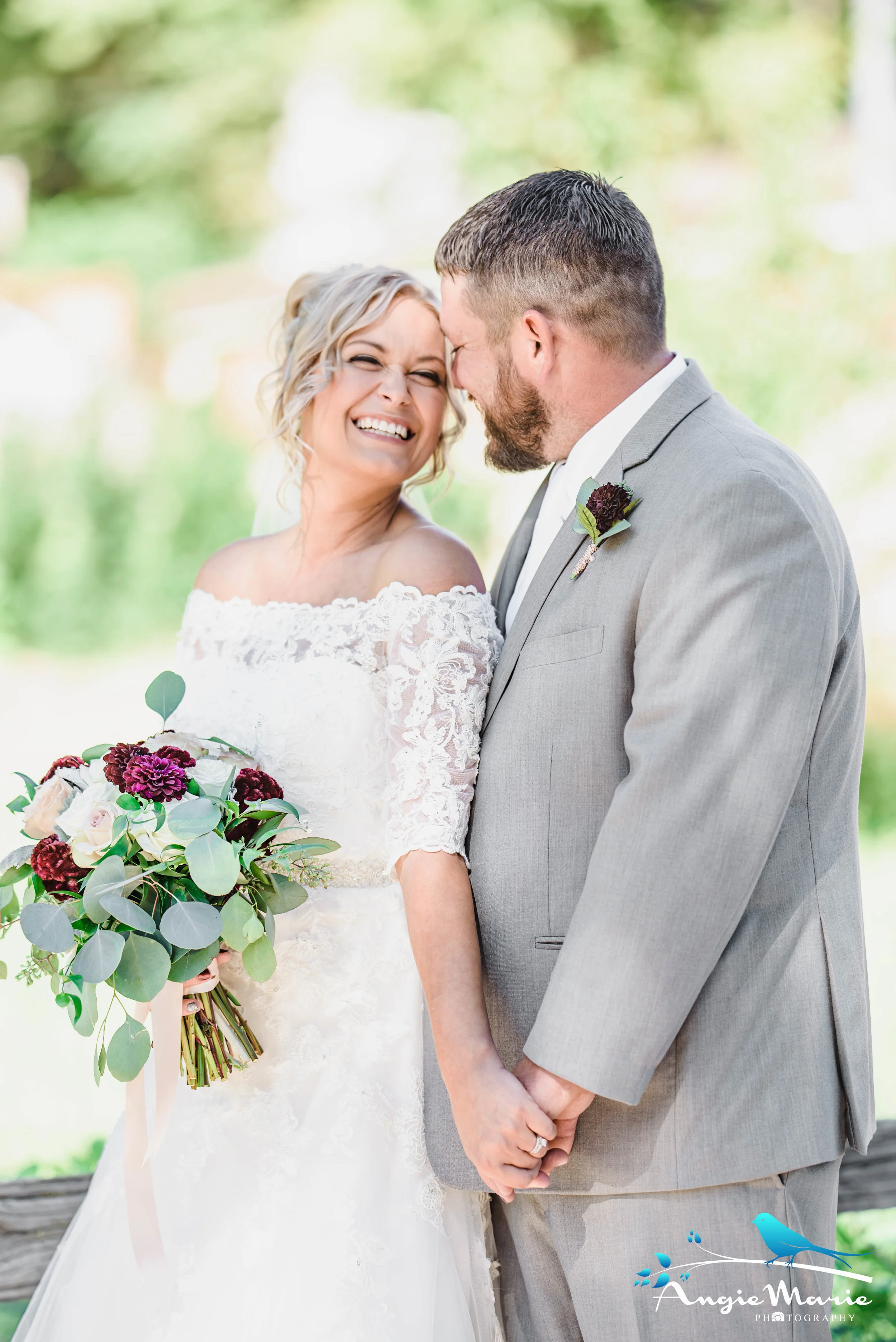 A bride and groom smiling and holding hands outdoors on their wedding day, with the bride holding a bouquet of flowers.