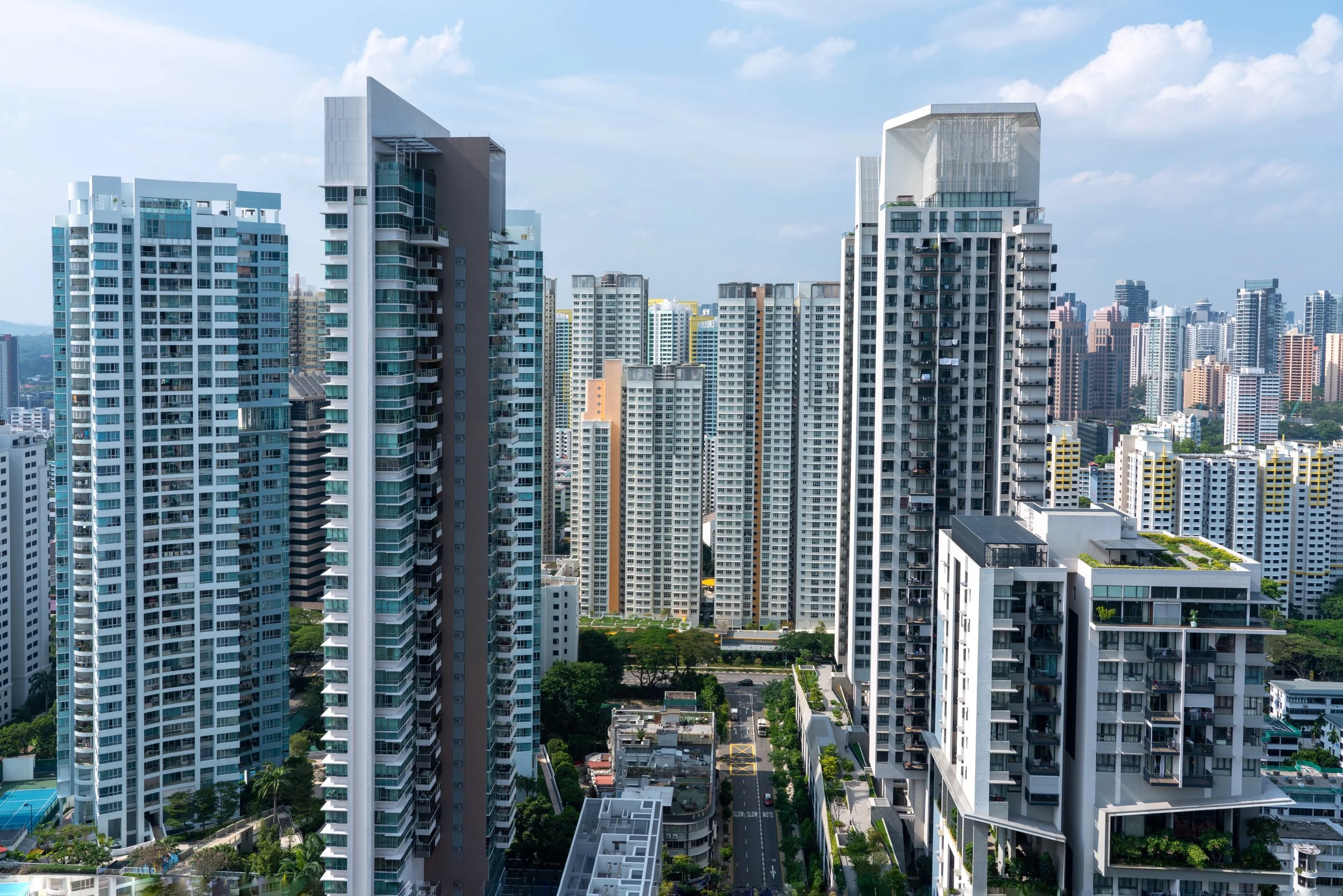 A cityscape featuring multiple modern high-rise apartment buildings under a partly cloudy sky.