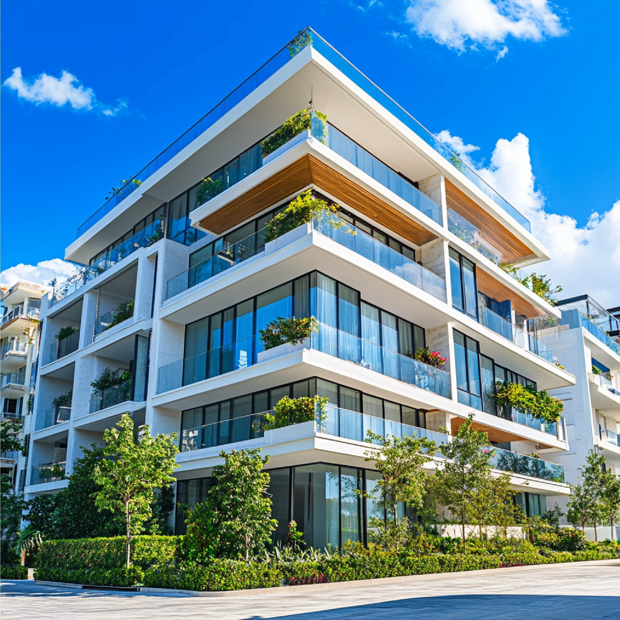 Modern white multi-story apartment building with glass balconies and green plants, under a blue sky with scattered clouds.