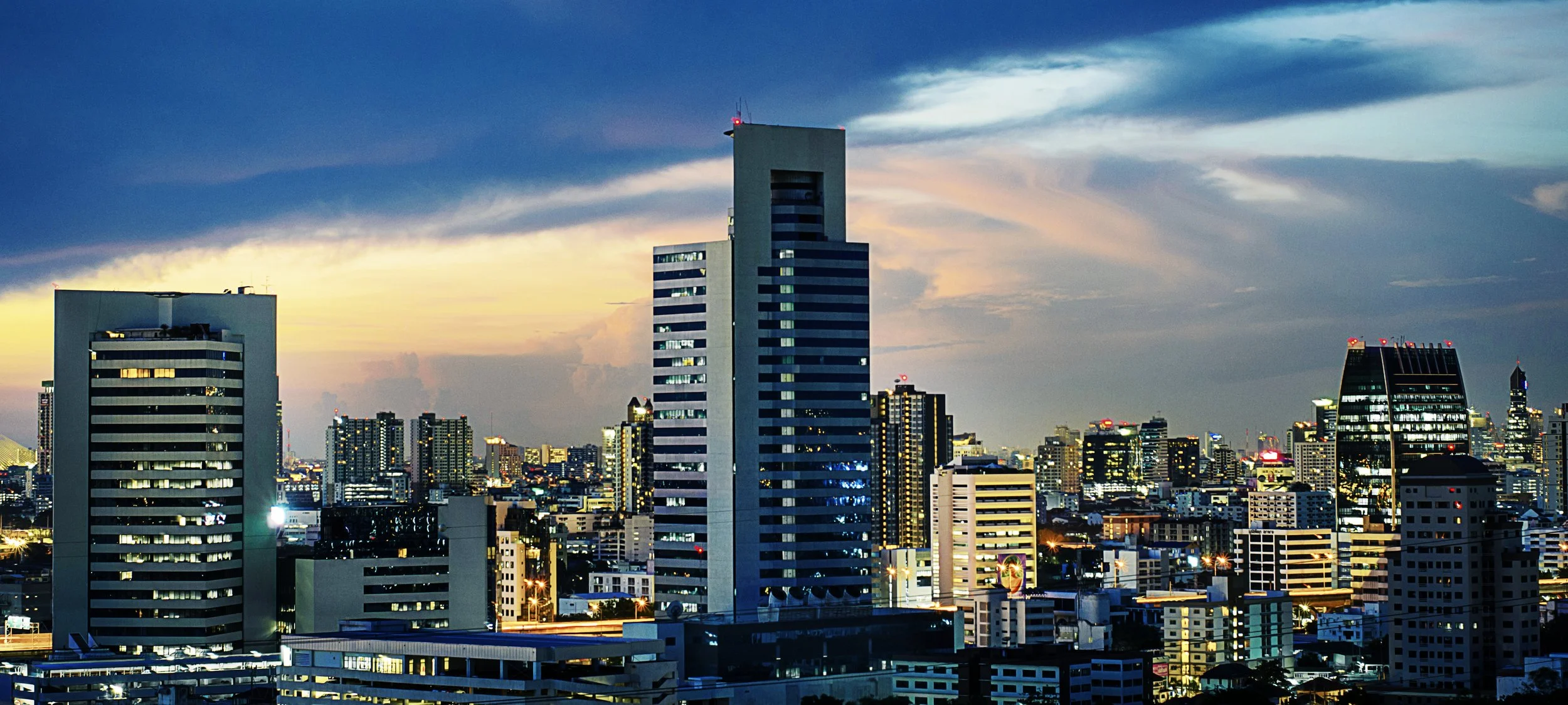 City skyline at dusk with illuminated skyscrapers and a colorful sky.