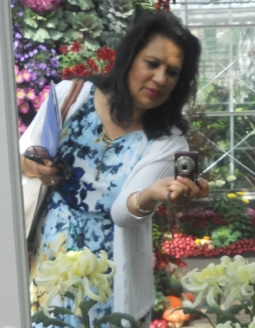 Woman taking a mirror selfie in a greenhouse surrounded by flowers and plants.