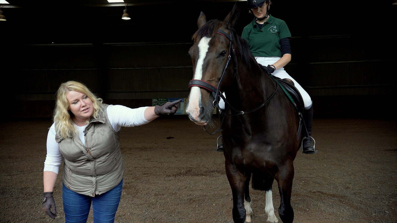 Phillipa Christie - Woman in white coaching a rider on a brown horse