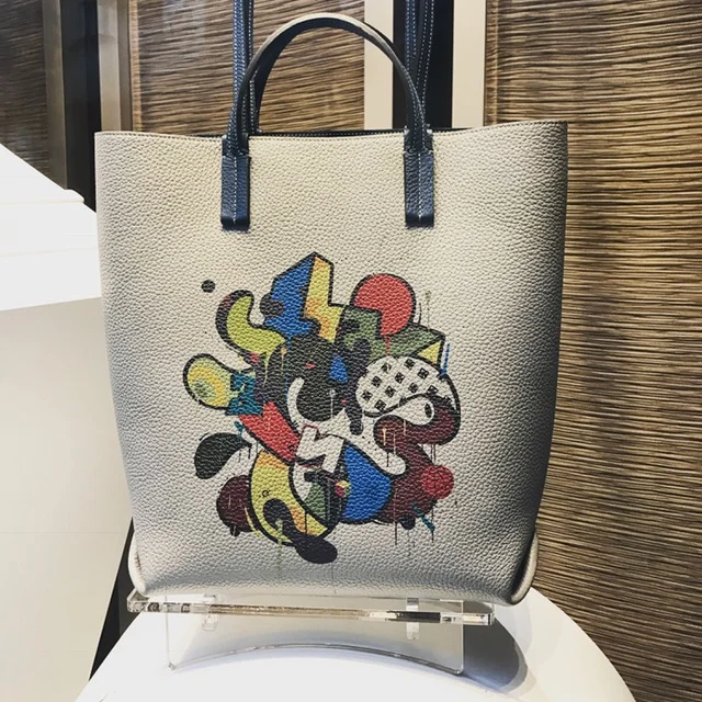 Moynat reached out to street artist, Mambo to create a whimsical collection combining his fluid artwork with the bags and accessories. The fun shopper above is completely reversible and has two handles, so it can carried a variety of ways.&nbsp;