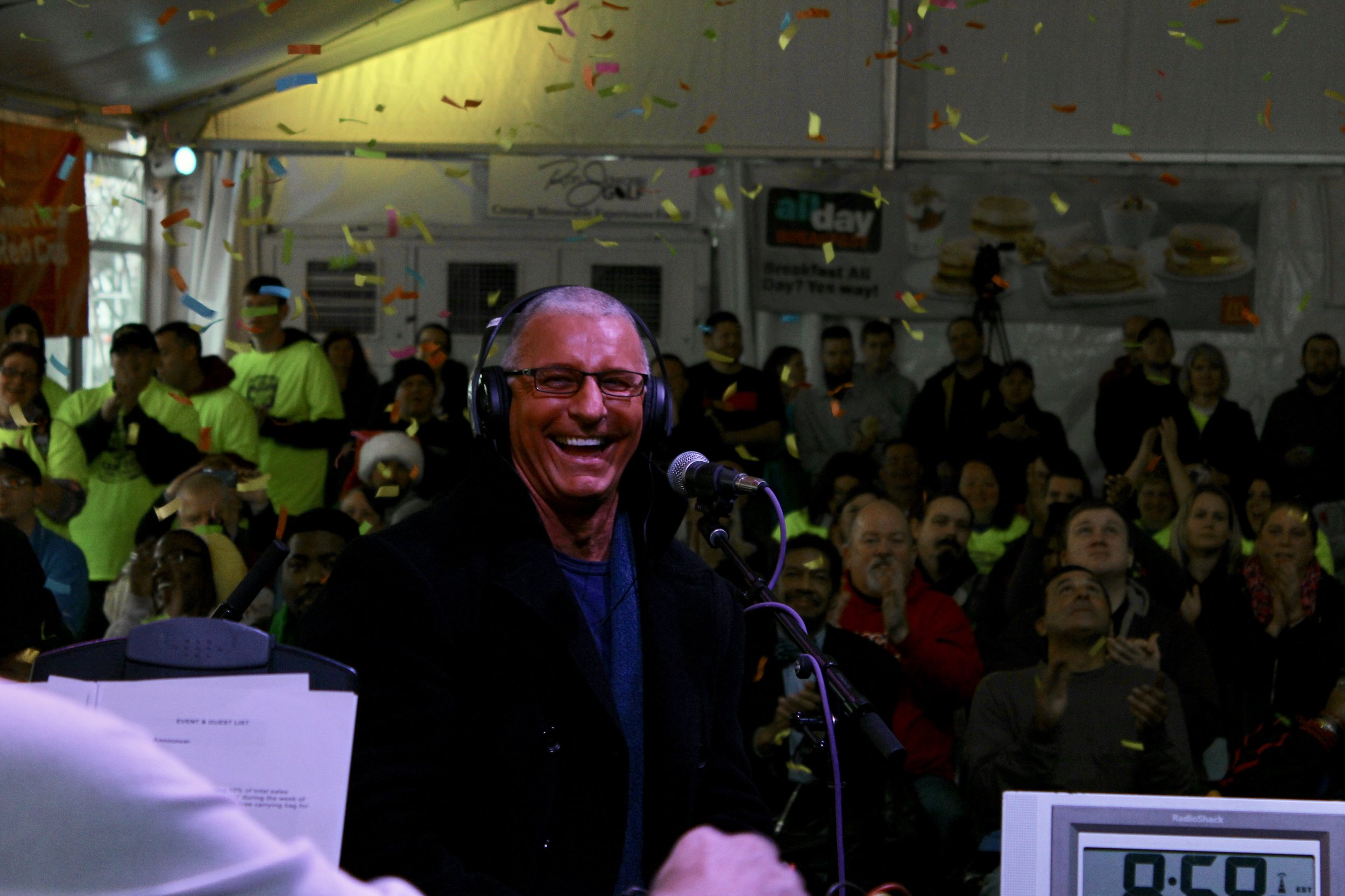 Alt text: famous english chef and tv personality robert irvine smiles with headphones on and a microphone in front of him as confetti drops down from above