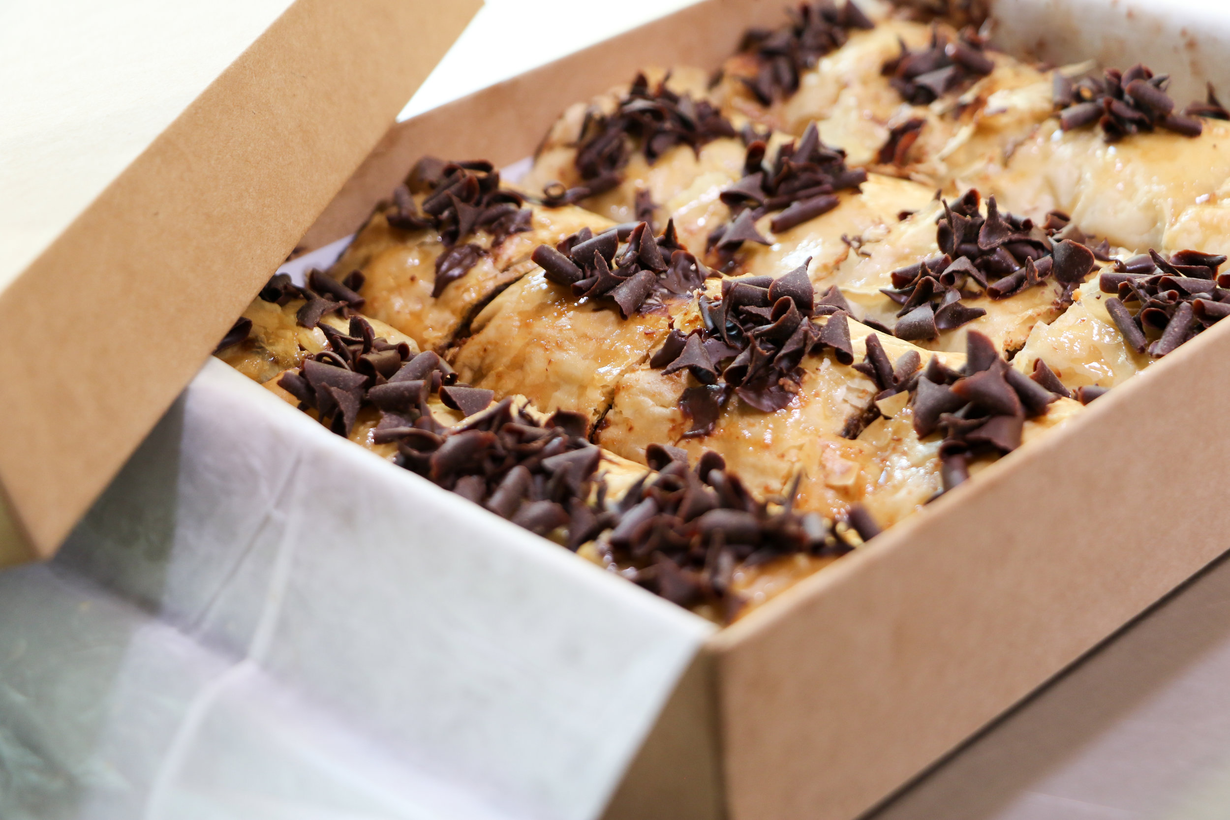 Alt text: peer into a brown cardboard box full of baklava with grated chocolate curls on top