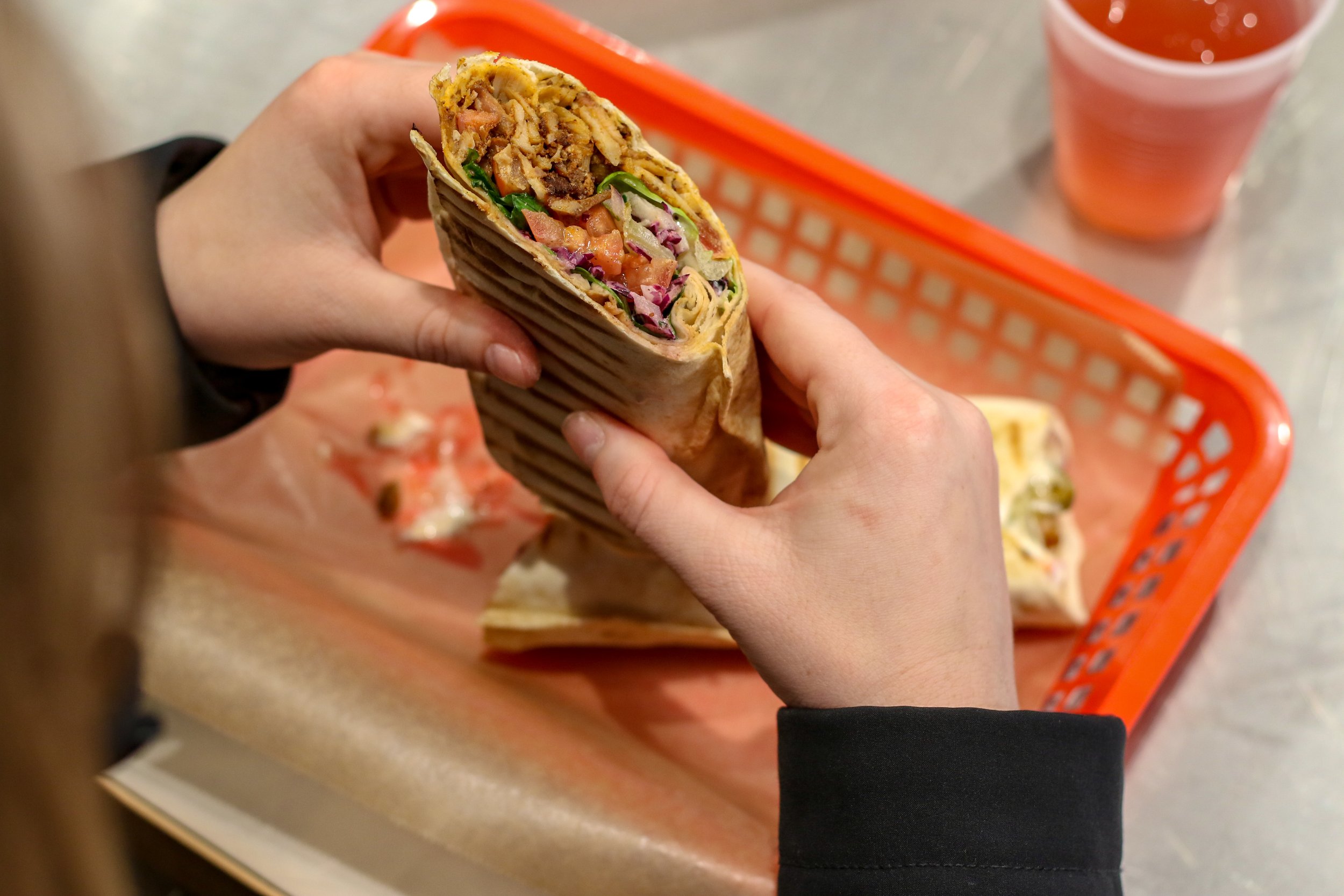 Alt text: a closeup of a falafel sandwich in pita wrap stuffed with meat, tomatoes, lettuce, onions and more.
