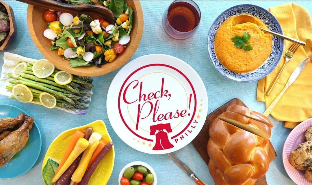 A colorful tablescape with food and dishes as well as red text that reads Check Please Philly!
