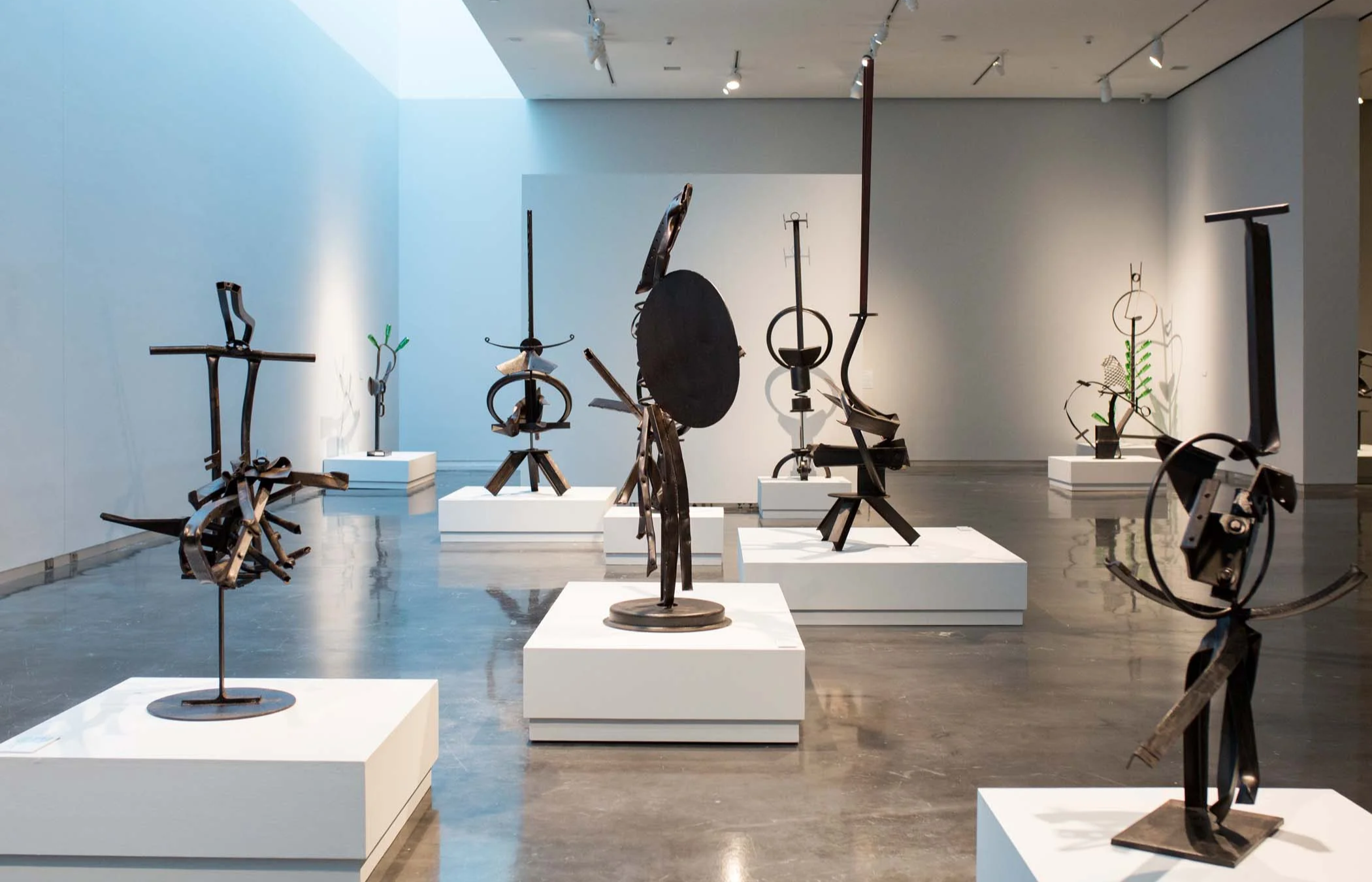 Gallery view of abstract metal sculptures by Martin Payton displayed on white pedestals, featuring geometric and organic forms across a polished concrete floor.