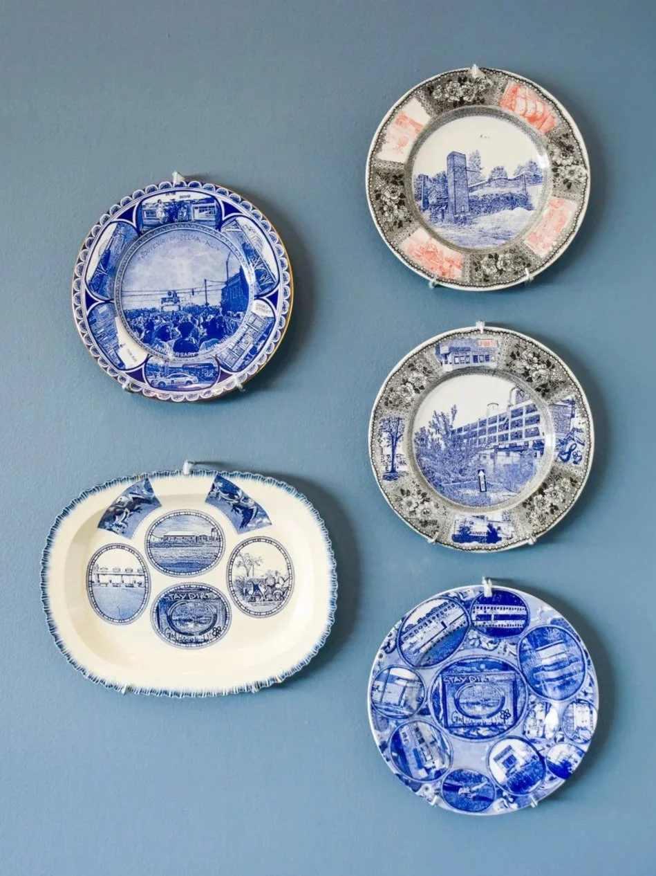 Five blue-and-white ceramic plates hang on a wall, each decorated with detailed printed scenes of buildings and landscapes in varying styles and compositions.