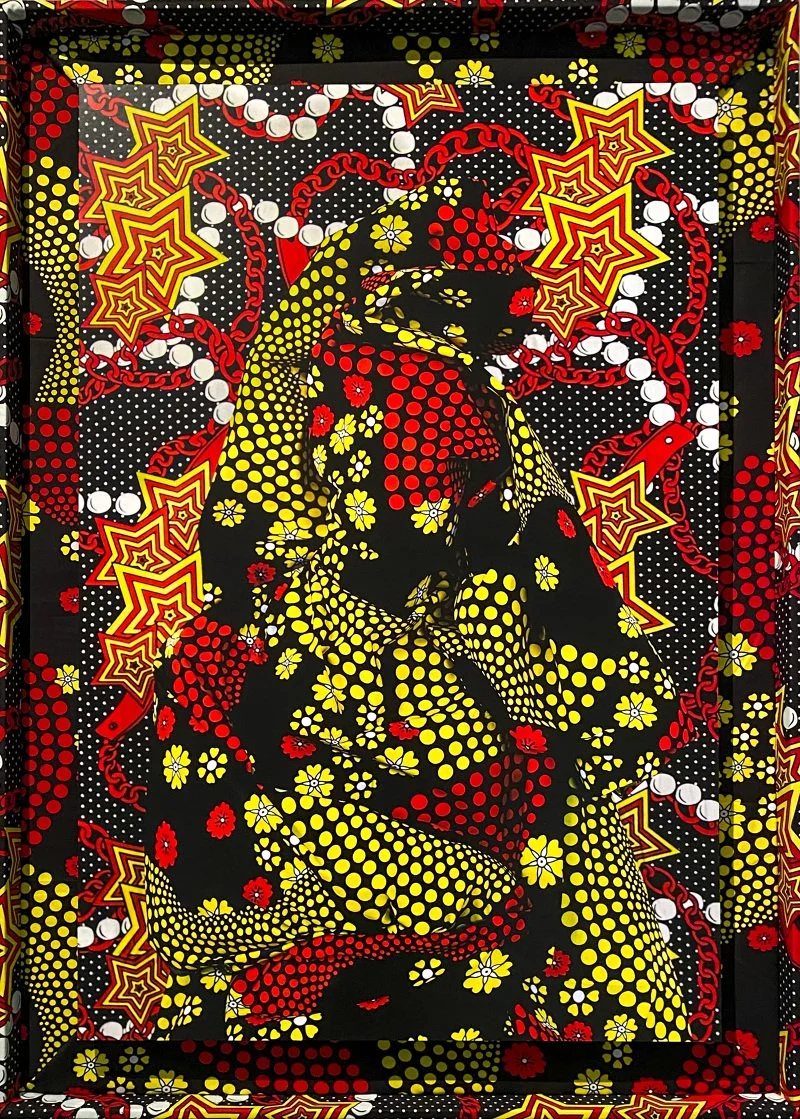 Vibrant textile-based artwork by Alia Ali featuring a seated figure rendered in bold red, yellow, and black patterned fabric with star and dot motifs forming the body and background. Atomic Flower by artist Alia Ali.