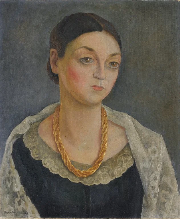 Portrait of a woman with dark hair parted at the center, wearing a dark dress, lace shawl, and gold necklace, set against a muted gray background. Caroline Durieux by artist Diego Rivera.
