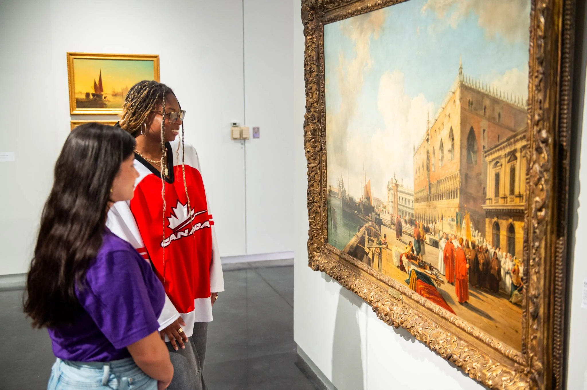 Two students looking at a painting of an Italian outdoor city scene.