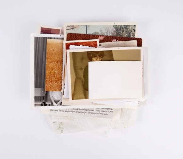A stack of old photographs on a white table by artist Kristine Thompson.