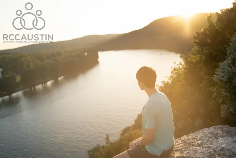 man sitting on rock looking down at river