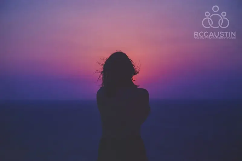 woman with arms over chest looking out at purple and pink sunrise