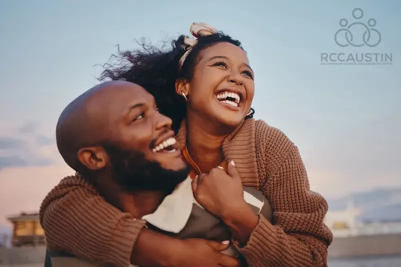 man giving woman piggyback at the beach both smiling widely