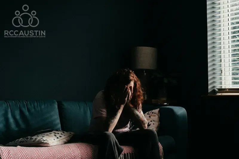 person sitting in dark living room with hands covering face
