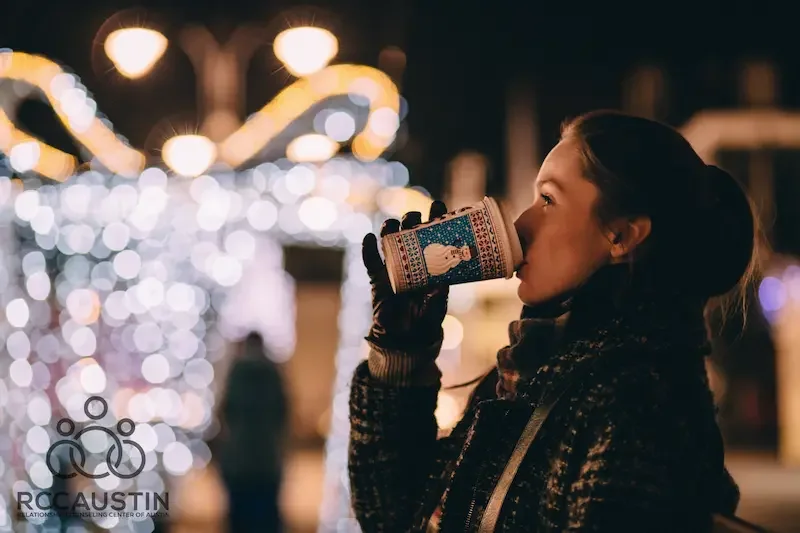 woman looking at holiday lights drinking hot drink