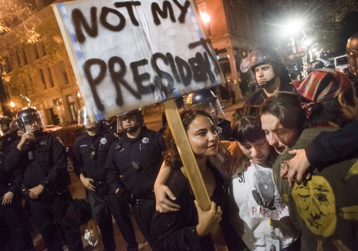Protesters embrace holding a sign that reads "not my president" as Oakland Police Department riot police attempt to break up an anti-Trump protest in downtown Oakland on November 9, 2016.