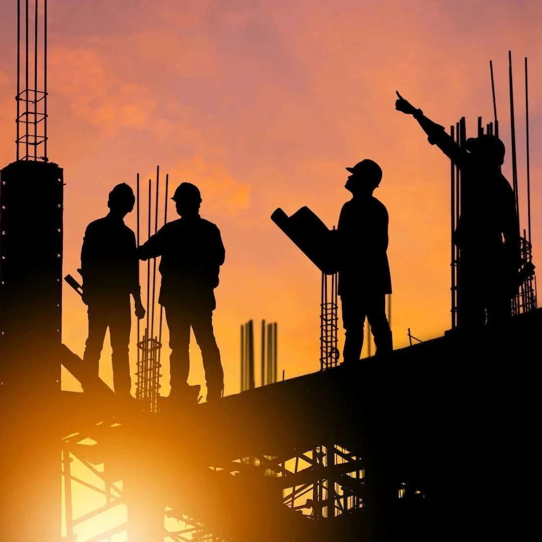 silhouettes of four construction workers standing on steel beams of a building under construction at sunset