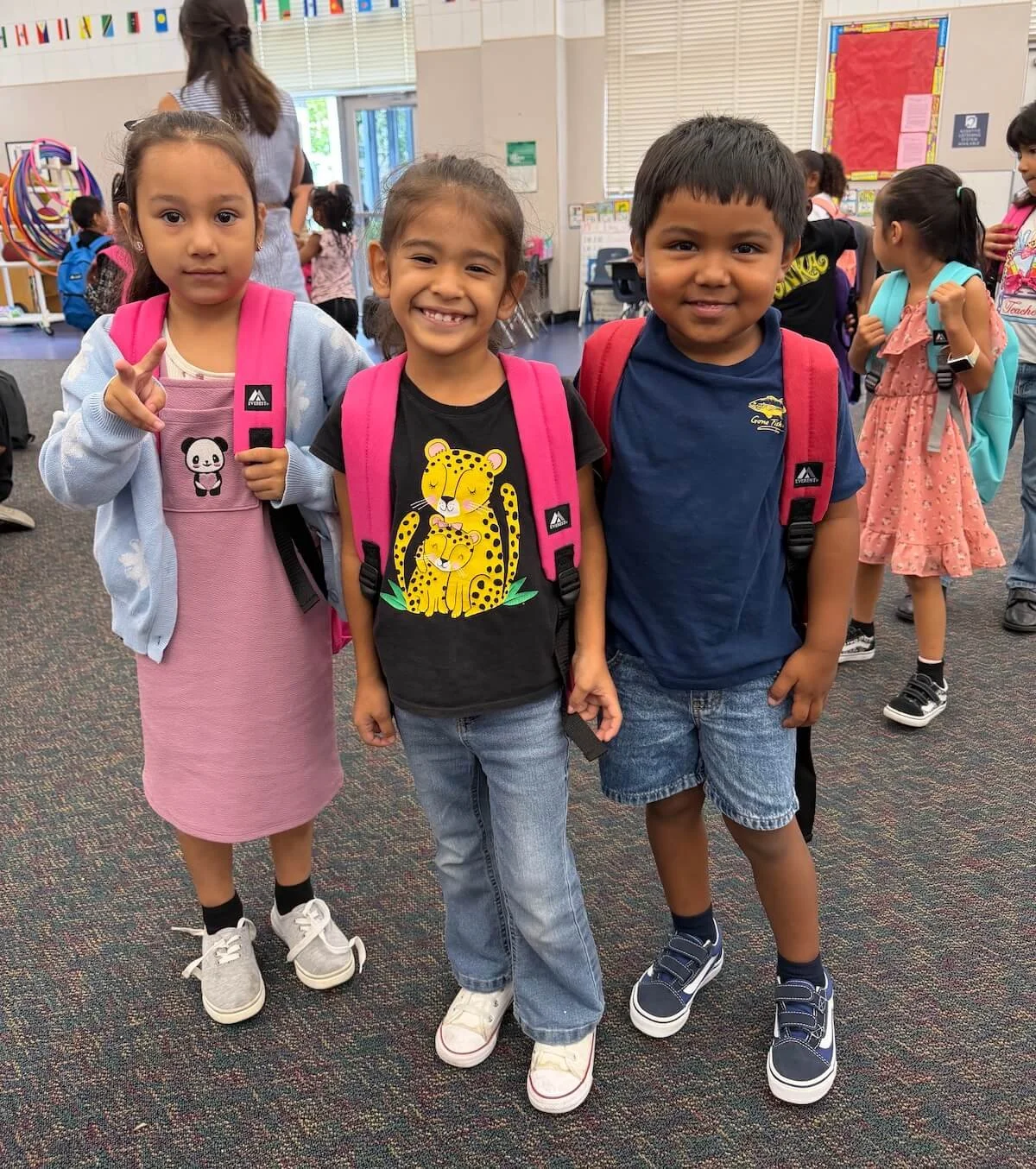 three young children smiling while wearing new backpacks provided by United Way of San Diego County