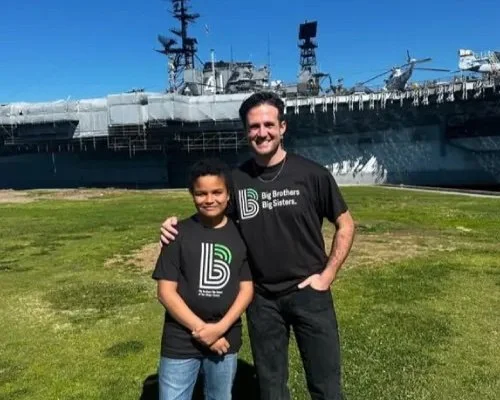 a mentor and child wearing Big Brother Big Sister of San Diego t-shirts standing in front of the Midway Museum ship