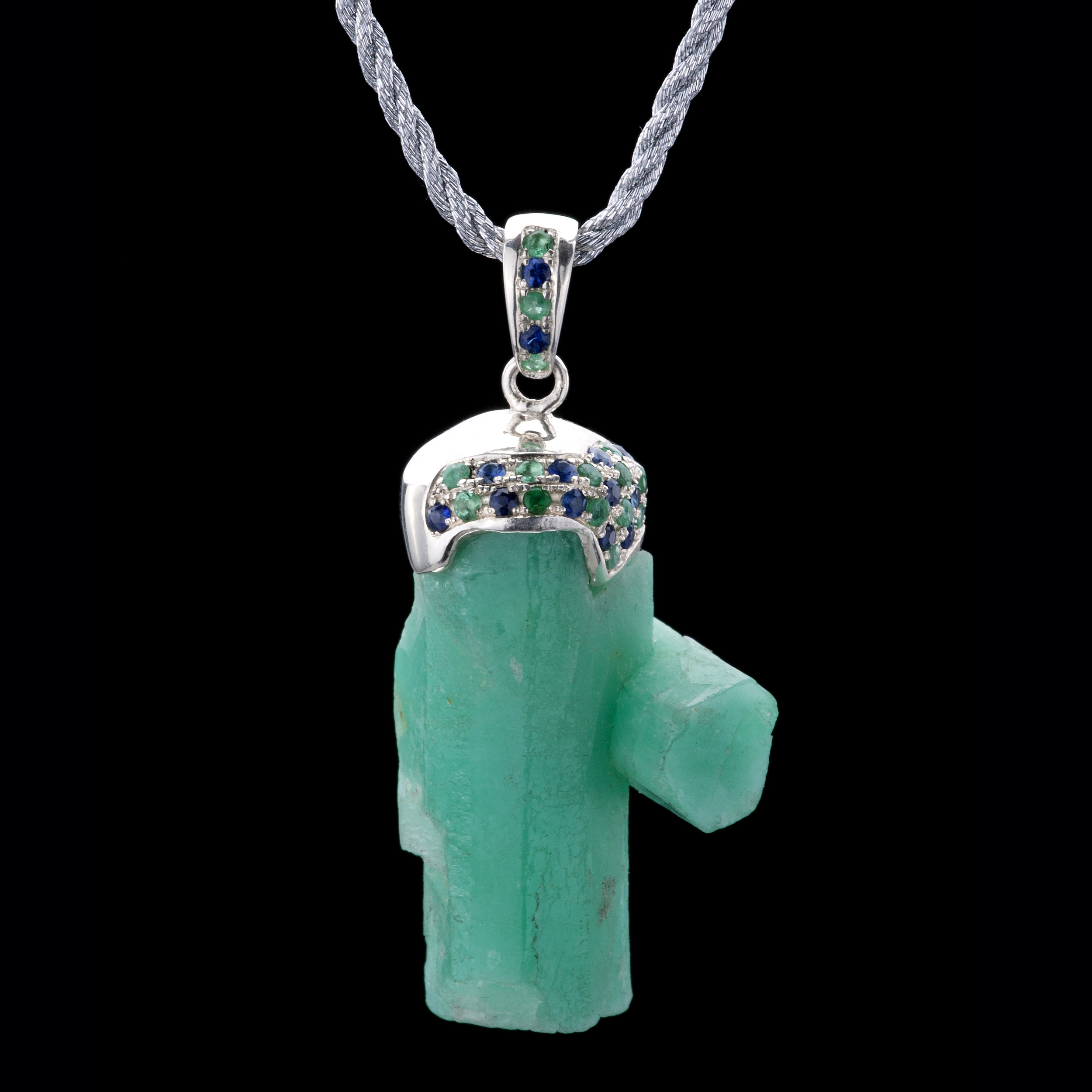A macle or unique double rough emerald crystals are embraced by sapphire and emerald pavé. Pendant is set in 925 silver