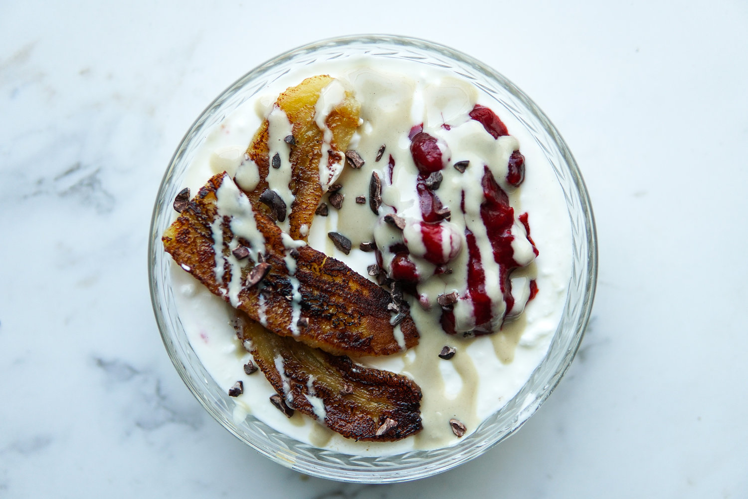Yogurt bowl with caramelized bananas, cranberry sauce, cacao nibs and tahini drizzle