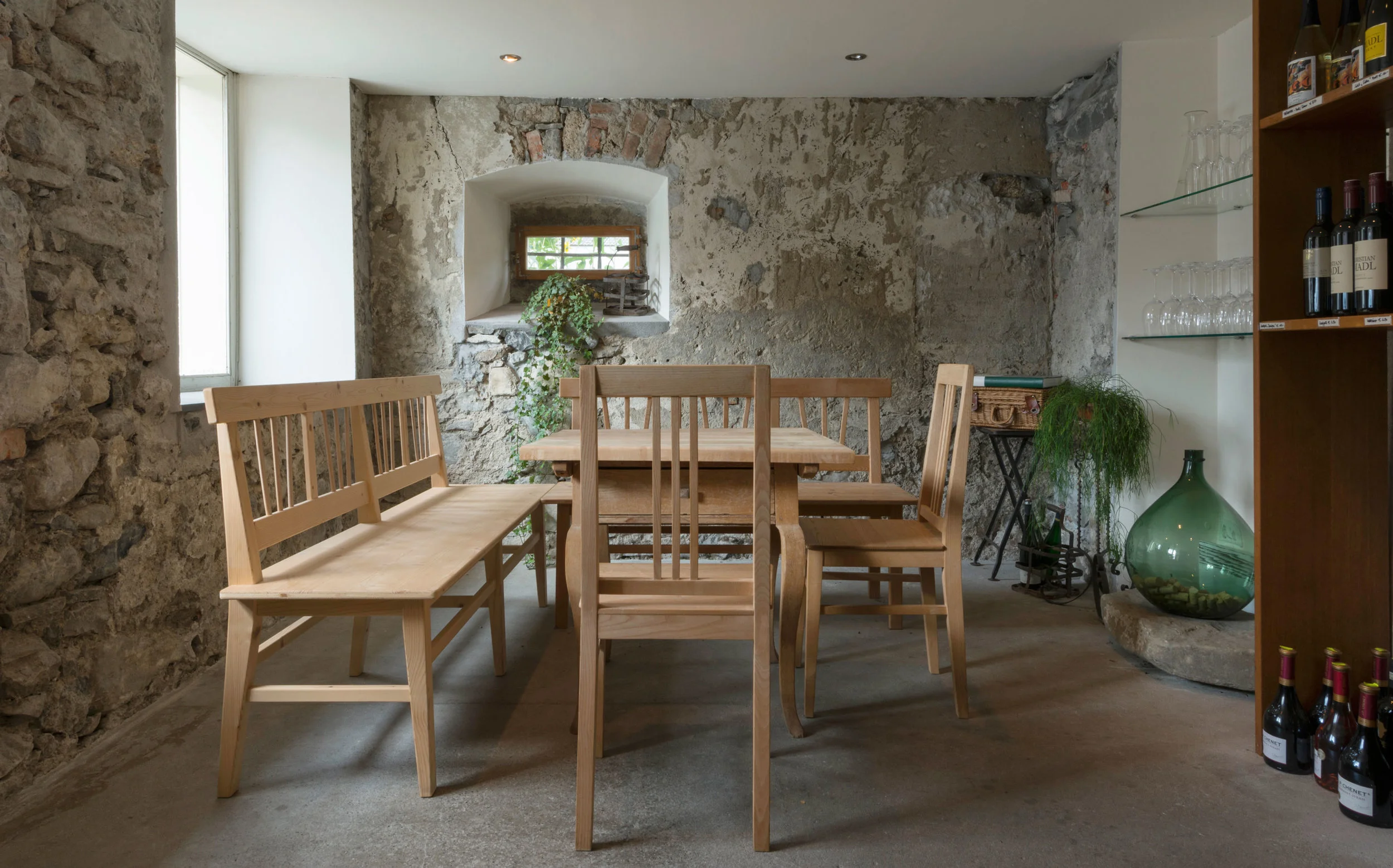 Blick vom Gang in den Weinkeller hinein. In der Mitte steht ein Holztisch mit zwei Bänken und zwei Stühlen die von Florian Berchtold – Hedis Ehemann – selbst gebaut wurden.