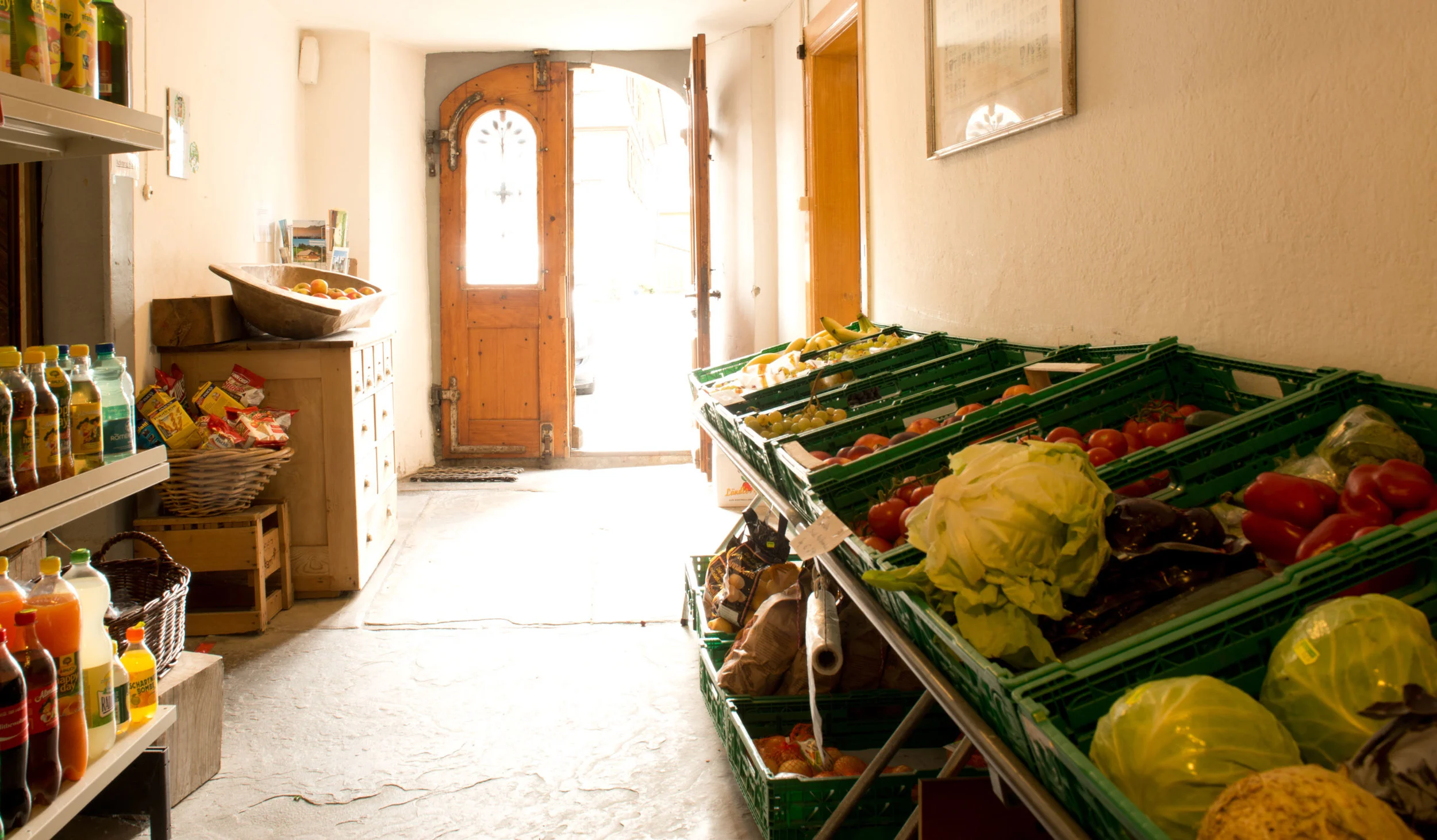 Der Blick durch den Gang des Ladens Richtung Eingang. Frisches Obst und Gemüse, einige Erfrischungsgetränke, Knabbergebäck und Postkarten sind hier zu finden. Links geht es in den Hauptraum mit Kassa, der dann weiter in den Käsekeller führt. Rechts geht ein Eingang in den Weinkeller.
