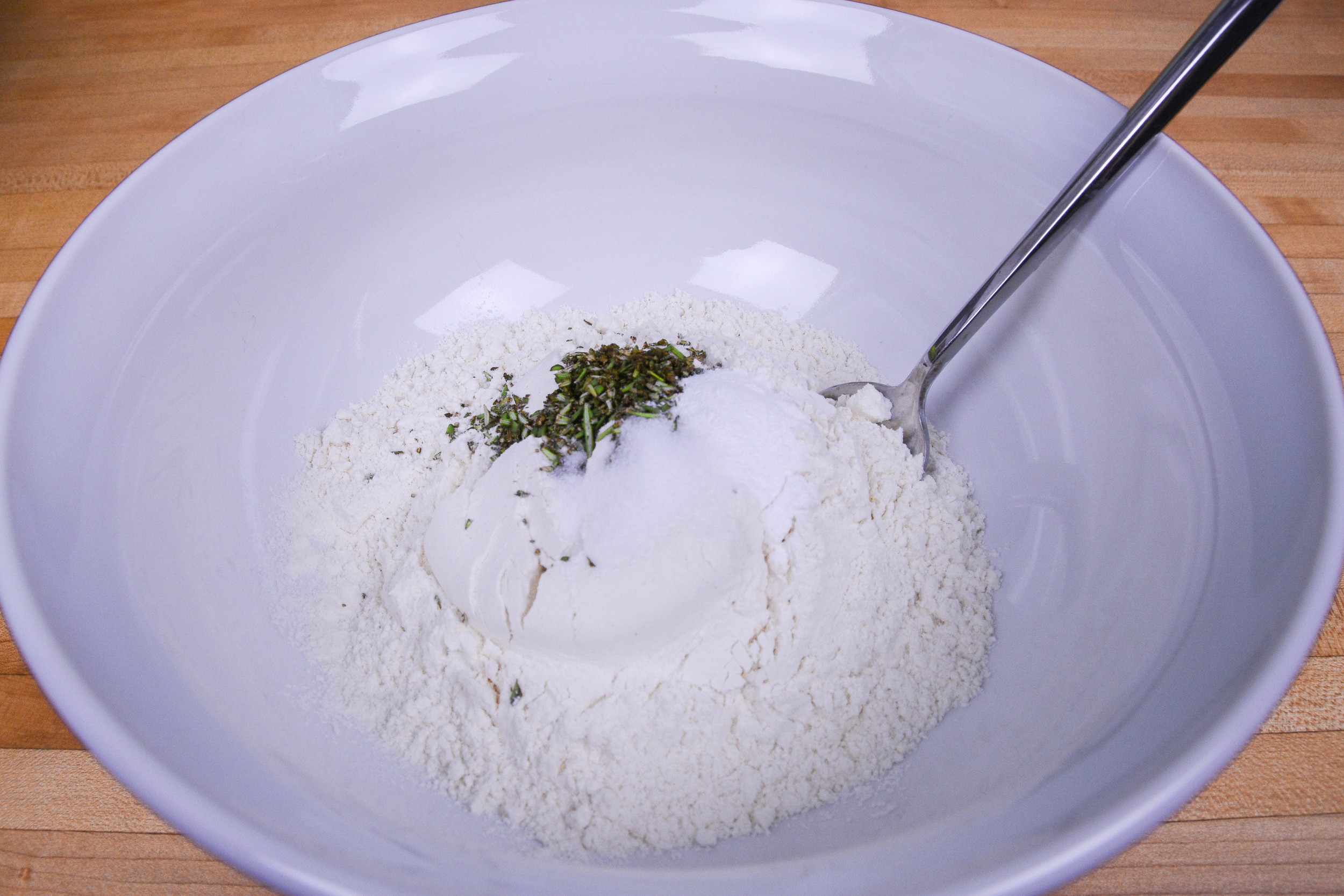 Preheat oven to 450 degrees. Finely chop 1 tablespoon of rosemary. Then, in a medium mixing bowl, combine flour, salt, baking powder, chopped rosemary and stir together. Once dry ingredients are mixed, create a well in the center and pour in olive oil and water. Slowly mix in dry ingredients with a wooden spoon until dough begins to form. Next, knead the dough 4-5 times. 